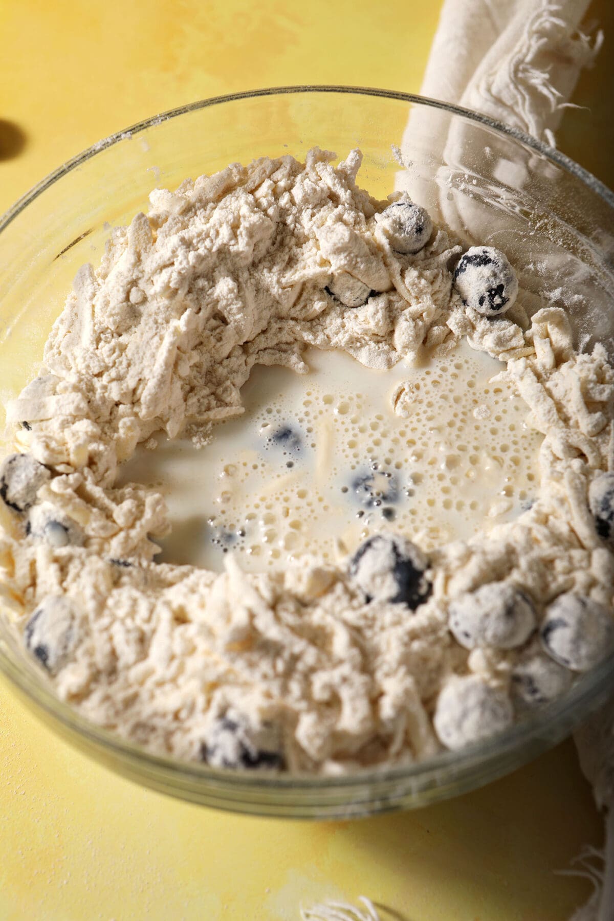 Milk in a bowl with blueberry biscuit ingredients before mixing