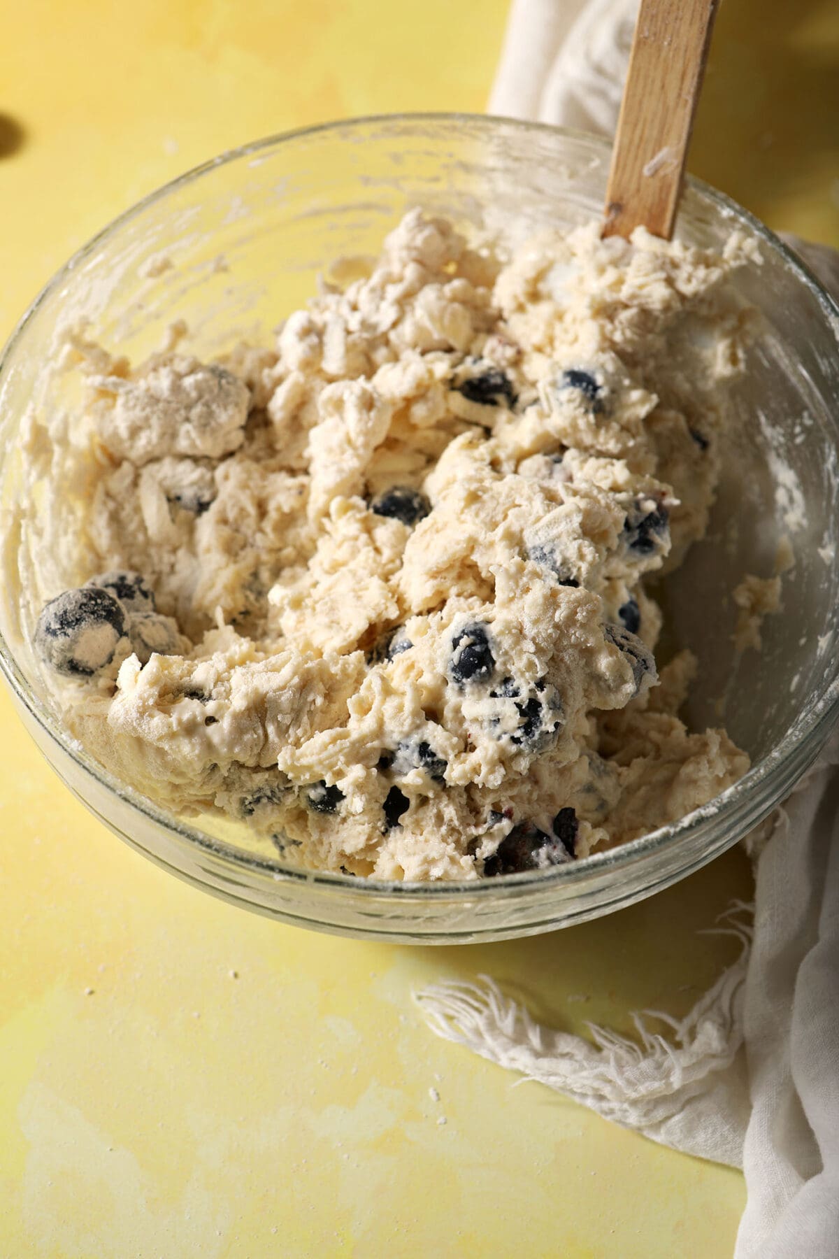 A shaggy biscuit dough with blueberries in a bowl on a yellow surface