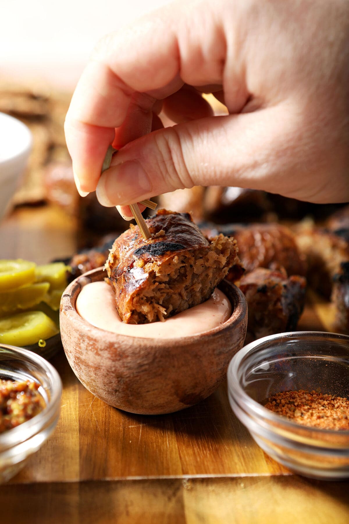 A hand dips a slice of boudin sausage into a dipping sauce on a cutting board