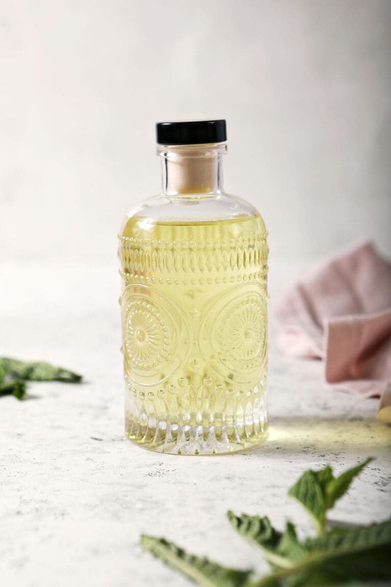 a bottle of mint simple syrup sits on a marble surface surrounded by mint leaves and a pink linen