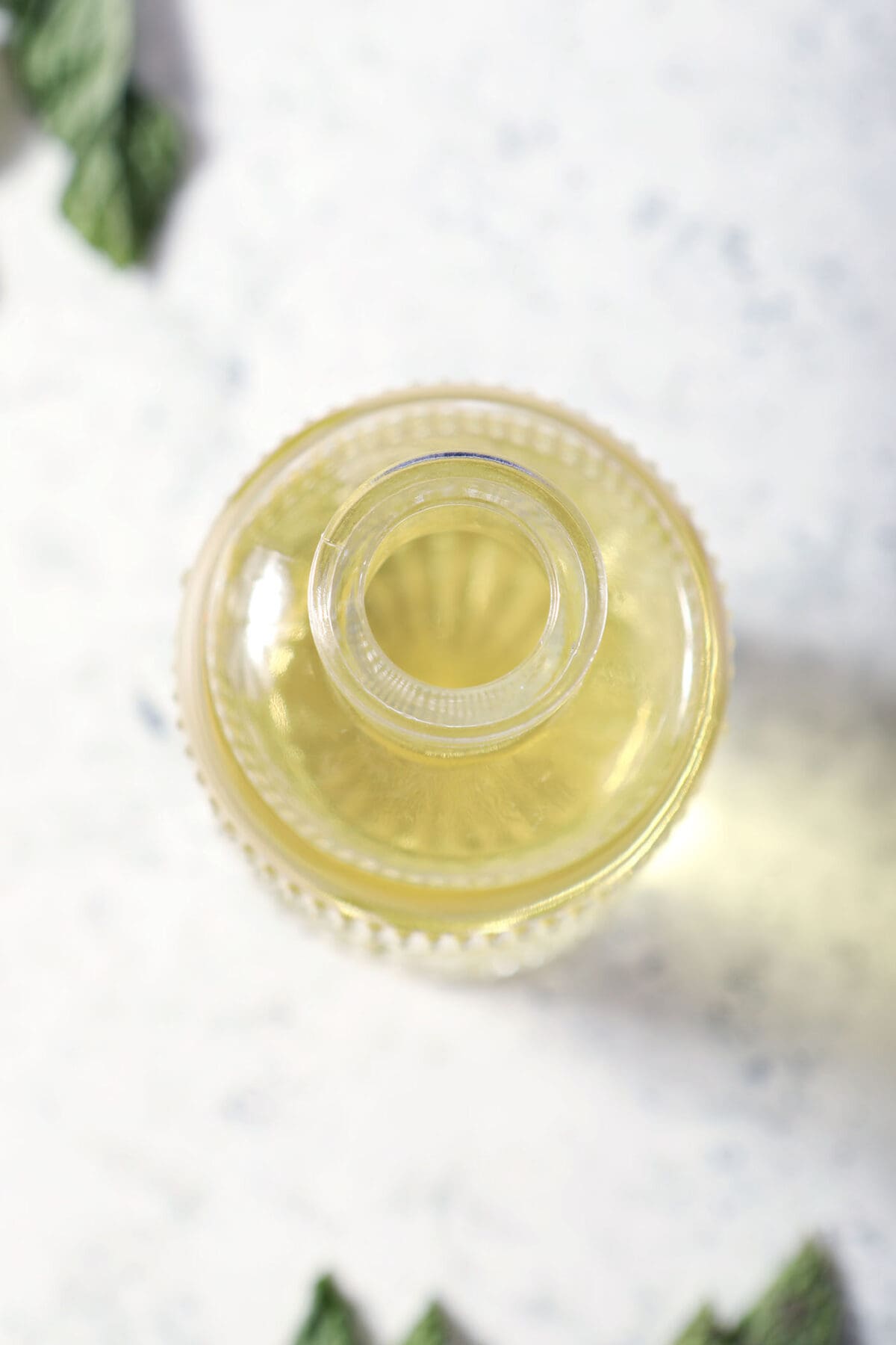 overhead of a fancy glass bottle of mint syrup on a stone surface surrounded by mint leaves