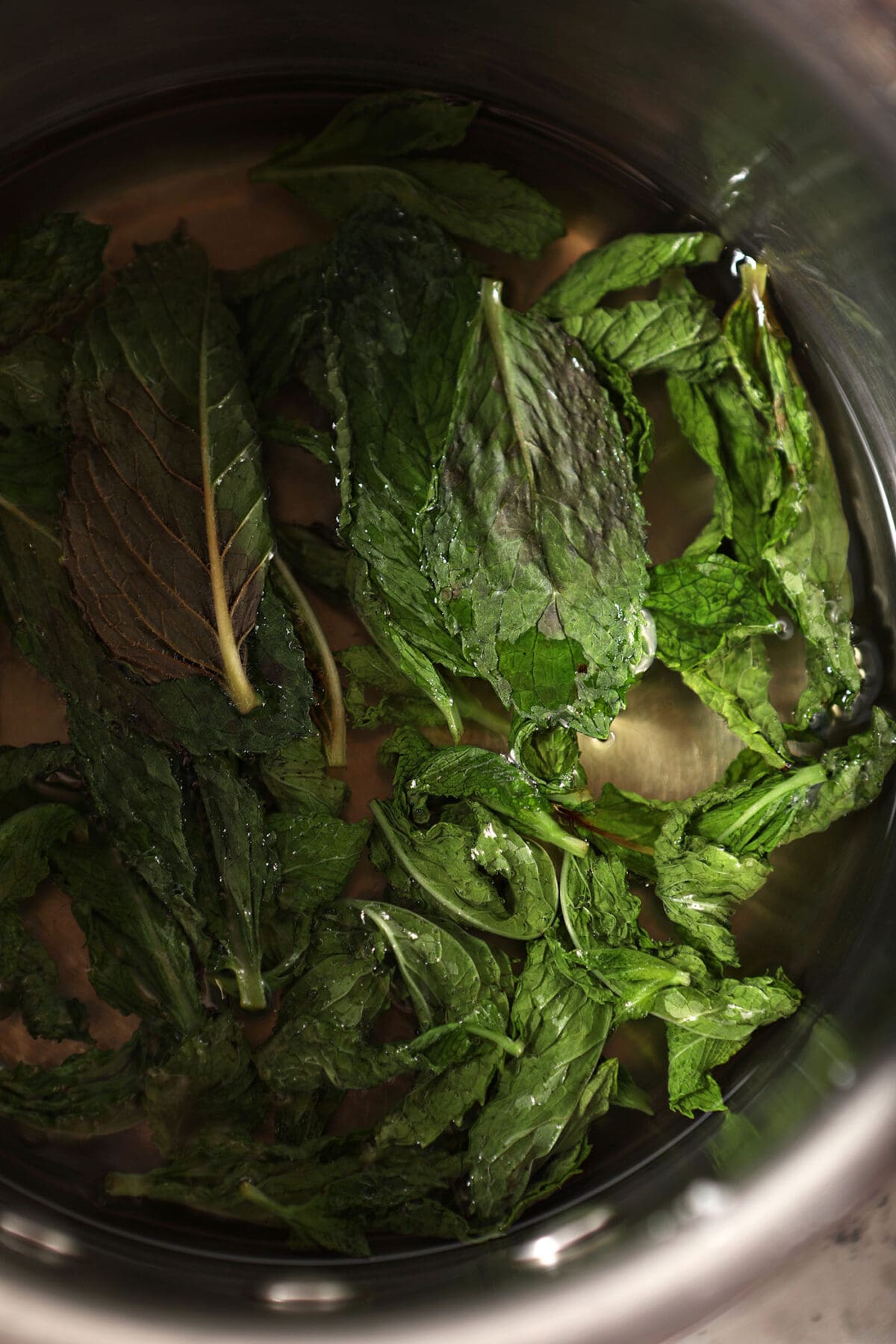 close up of mint leaves infusing in a saucepan of simple syrup