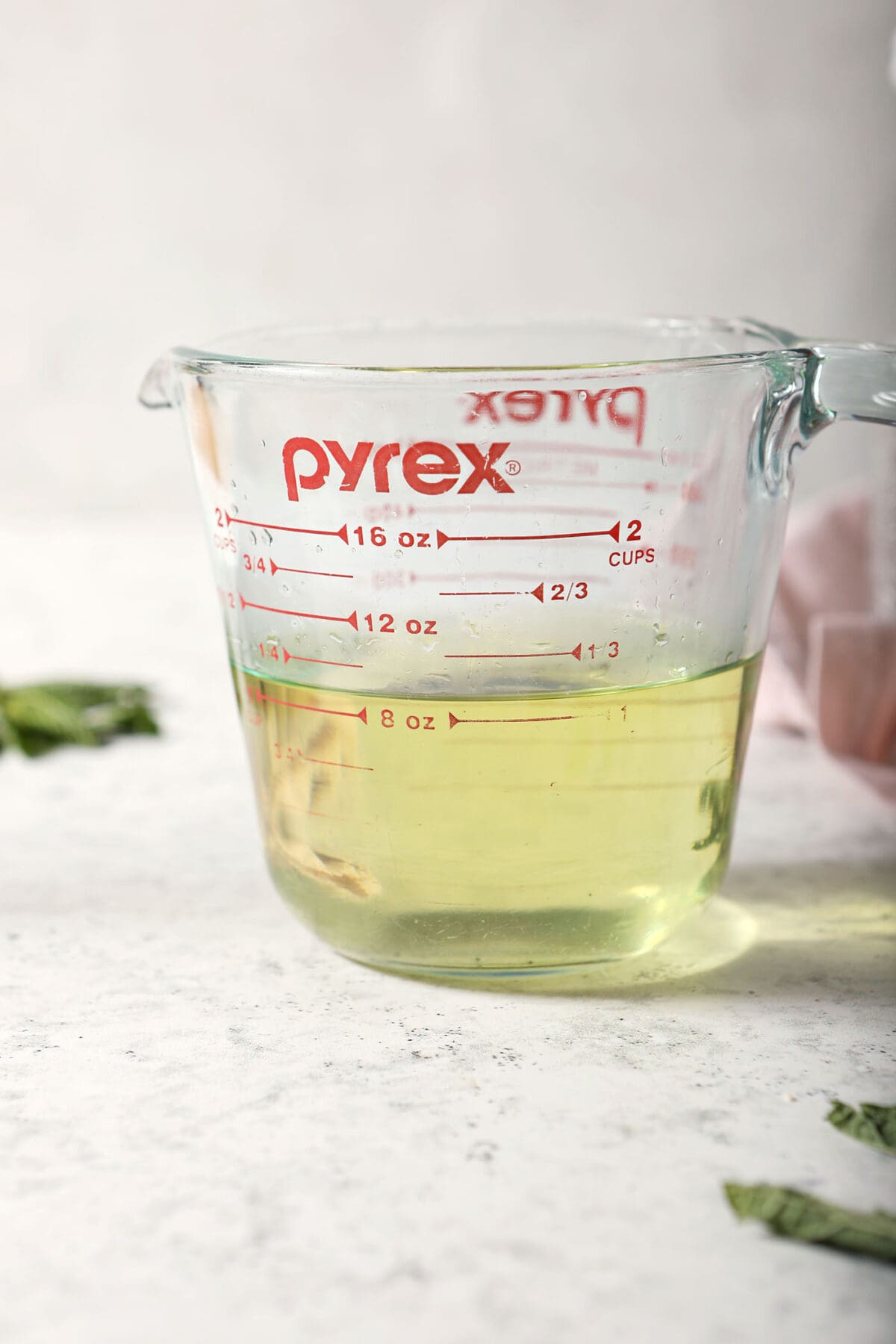 a liquid measuring cup of mint simple syrup on a stone surface