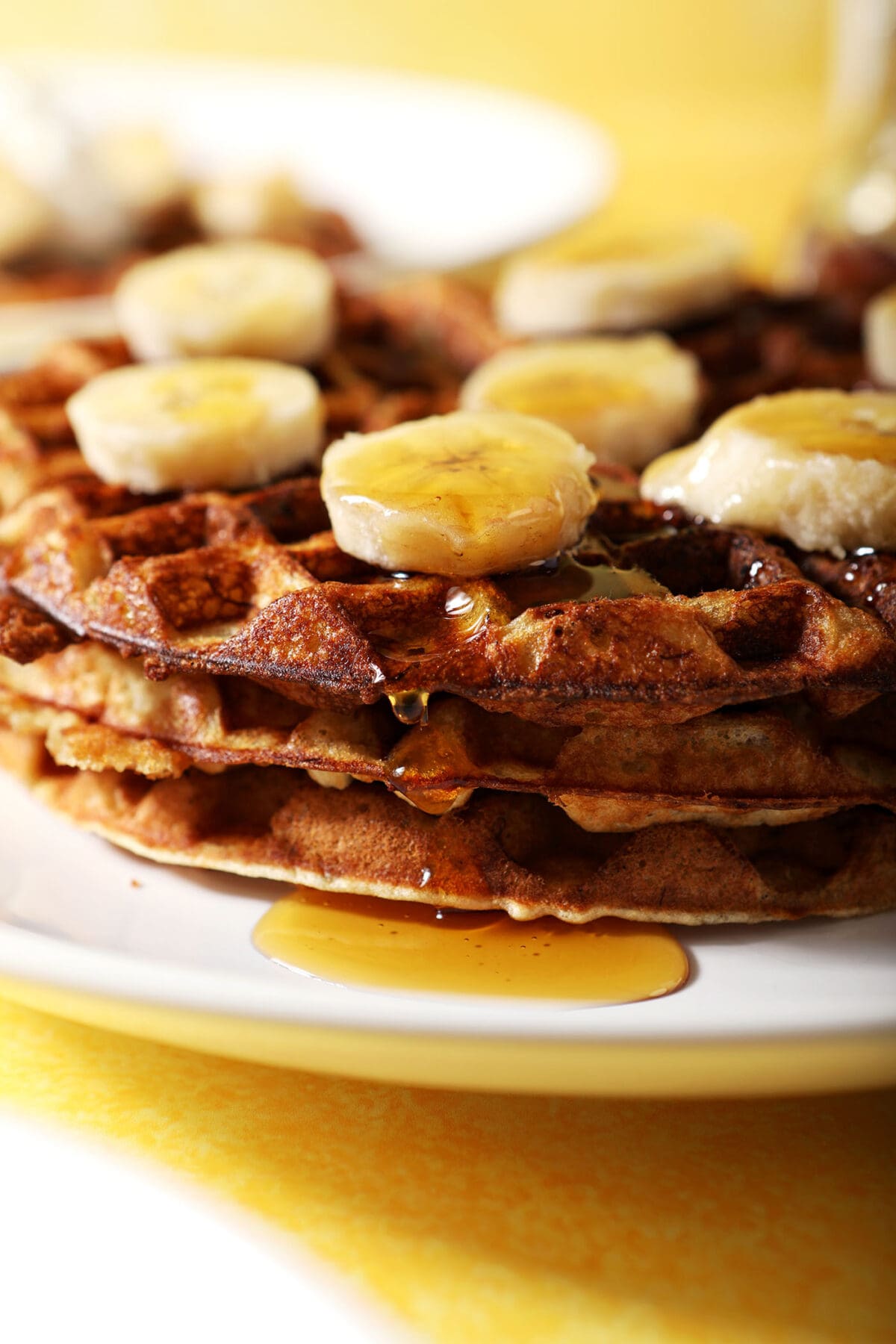 Close up of three waffles stacked with bananas and maple syrup on top on a white plate
