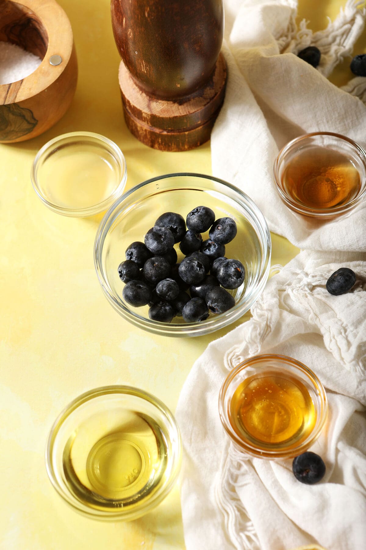 Ingredients to make a salad dressing with blueberries on a yellow surface with a white linen