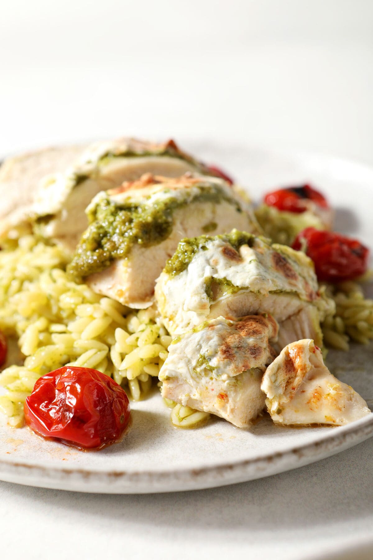 Side view of a sliced caprese chicken breast on top of pesto pasta with roasted tomatoes