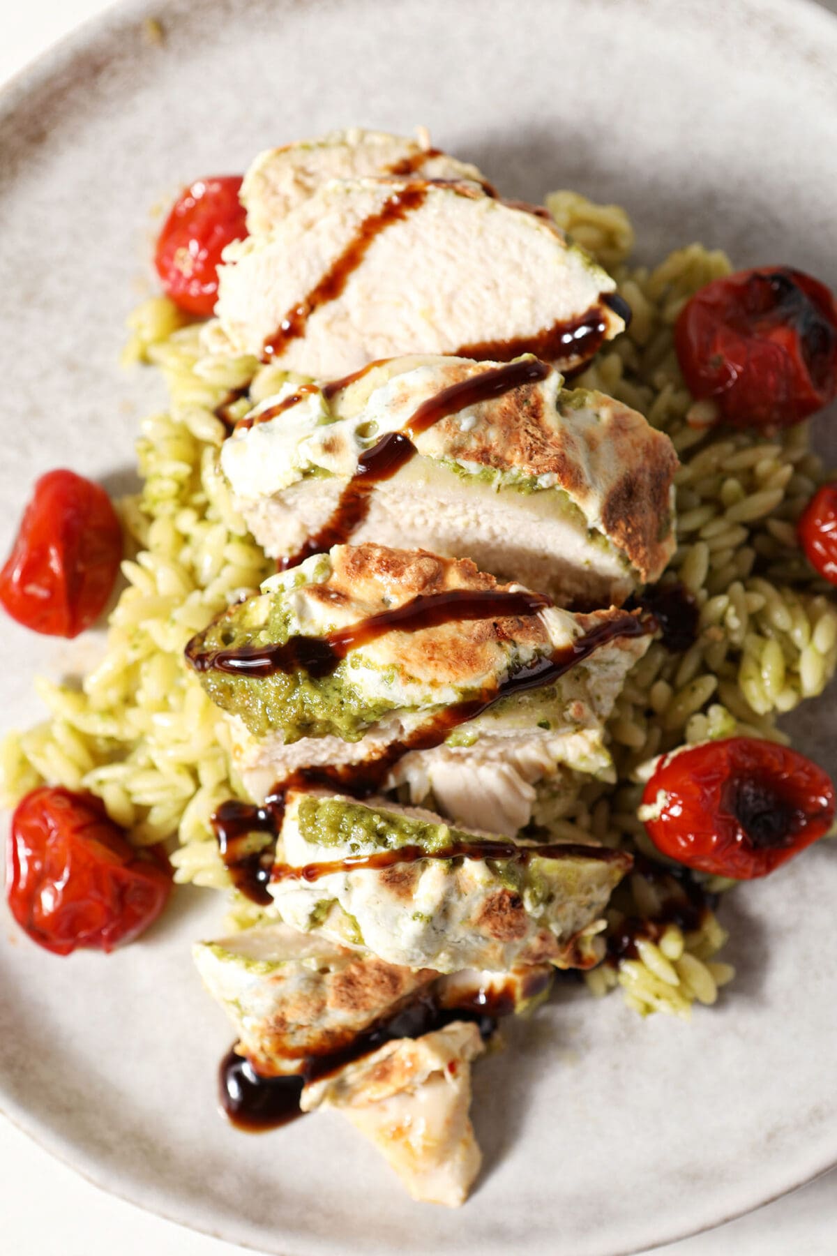 Close up of caprese chicken drizzled with balsamic, served with roasted tomatoes and pesto pasta