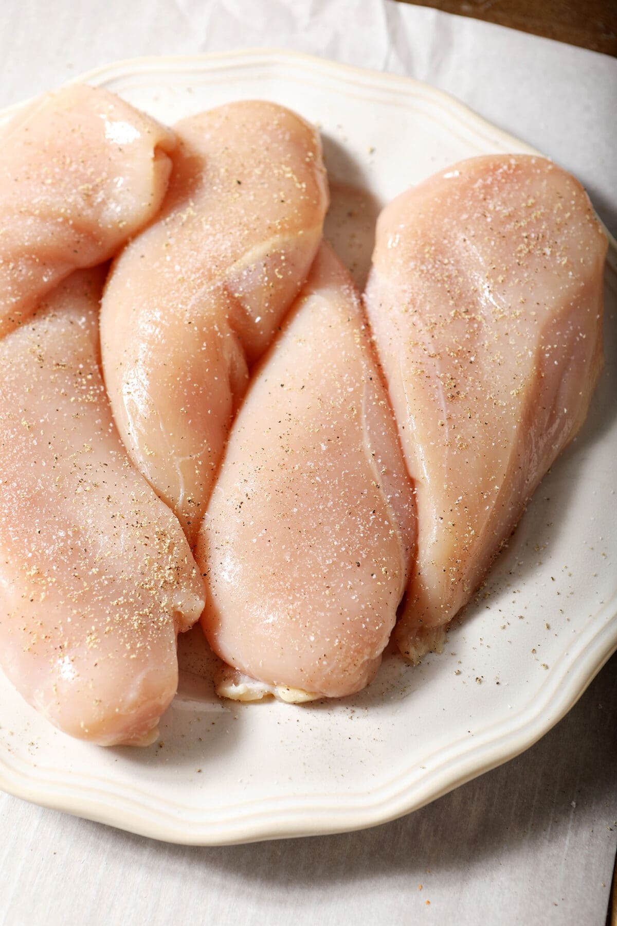 Raw chicken breasts on a white plate seasoned with salt and pepper