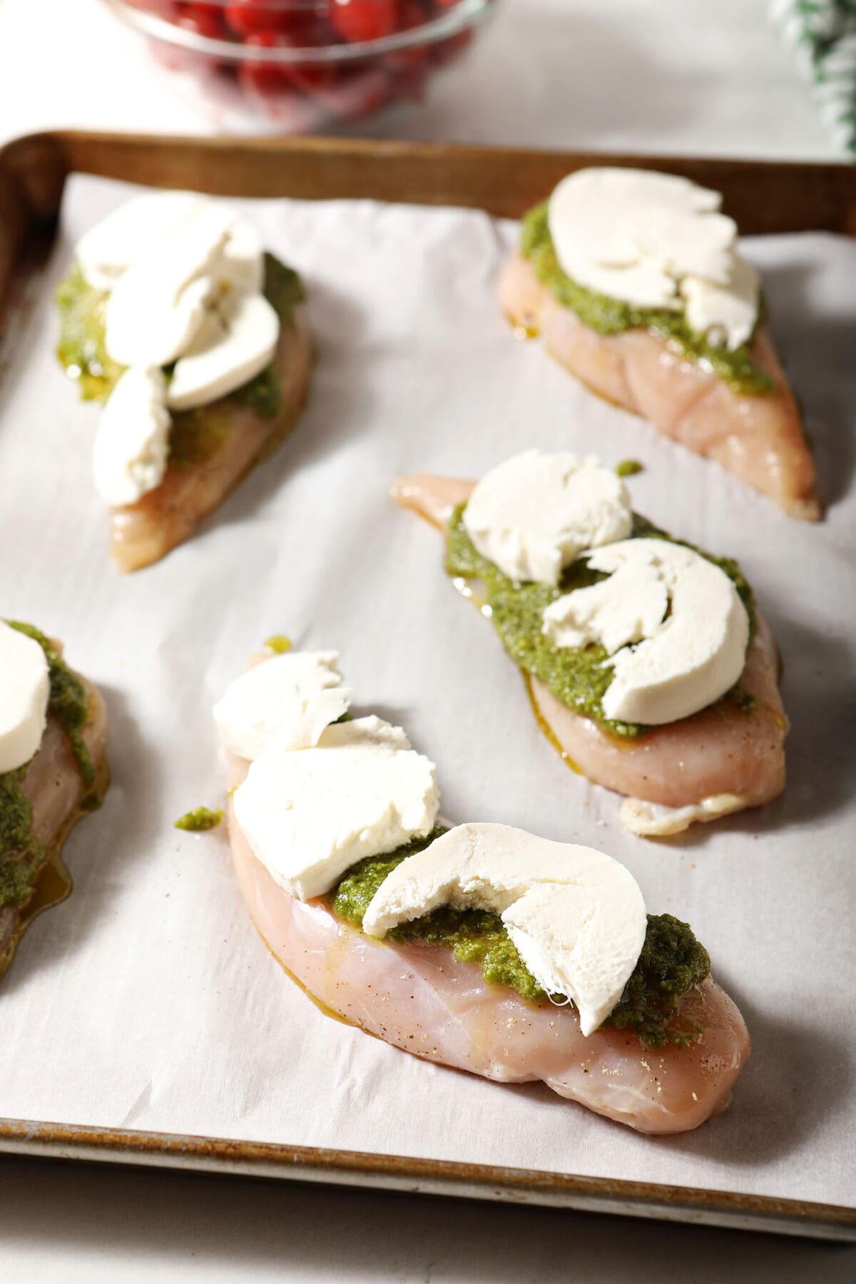 Slices of fresh mozzarella on chicken breasts with pesto on a sheet pan