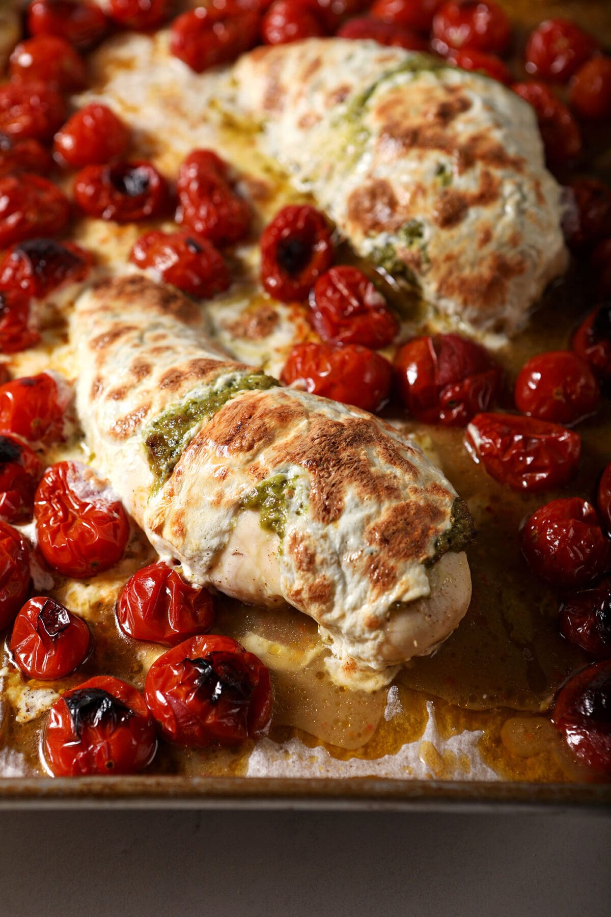 Roasted chicken breasts with melted mozzarella on top with roasted tomatoes on a sheet pan