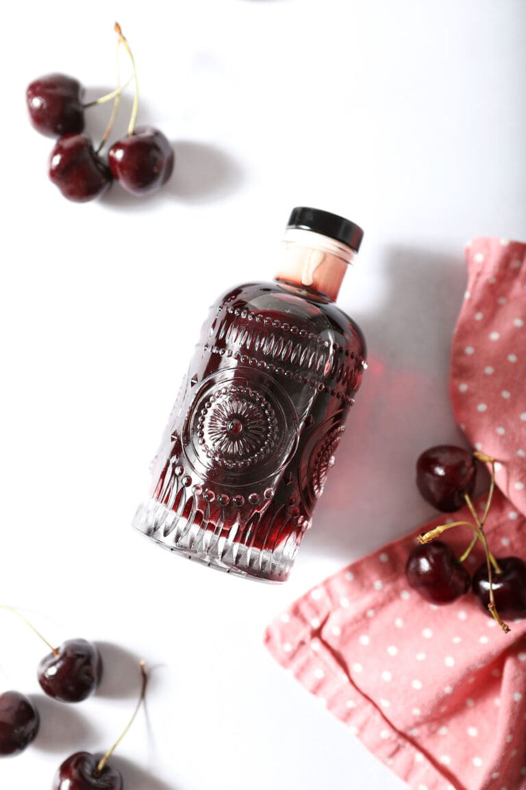 A bottle of cherry simple syrup on its side next to fresh cherries and pink polka dot linen