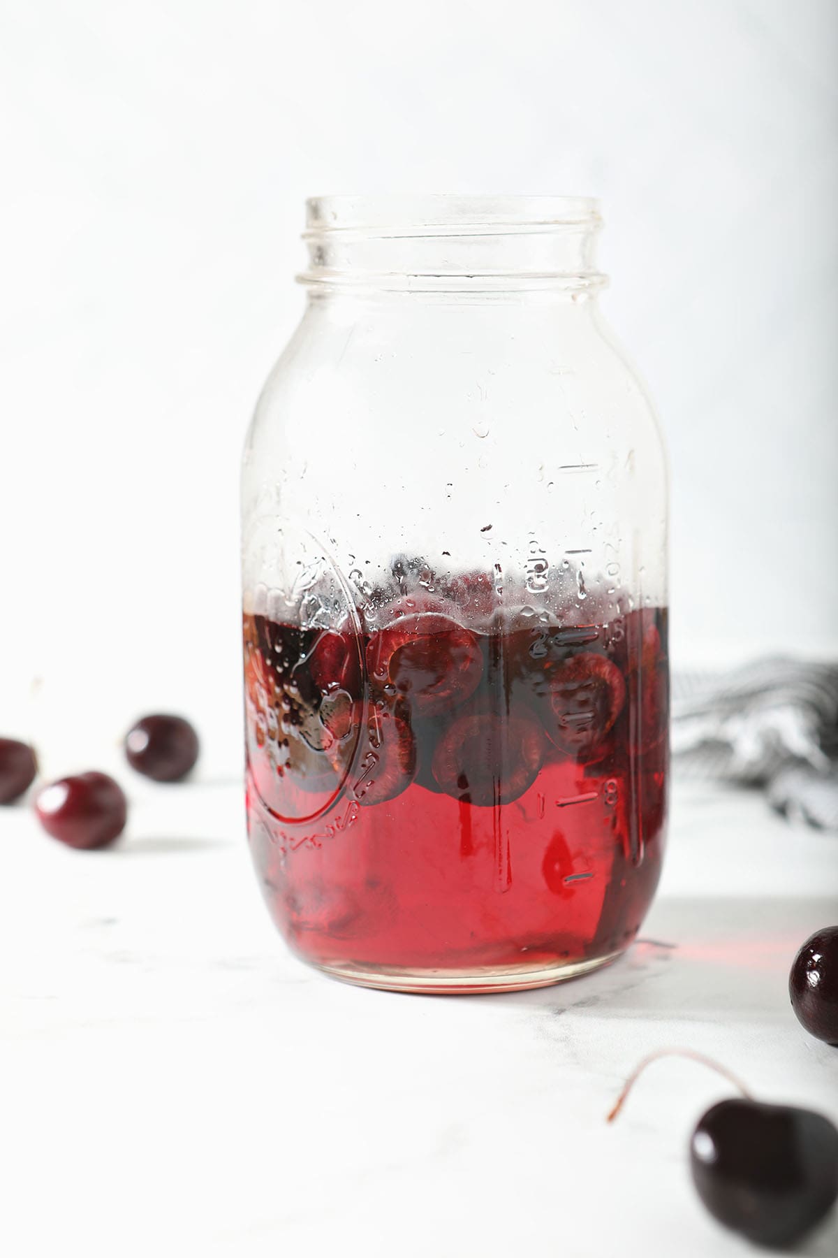 A mason jar of cherry simple syrup with halved cherries in it