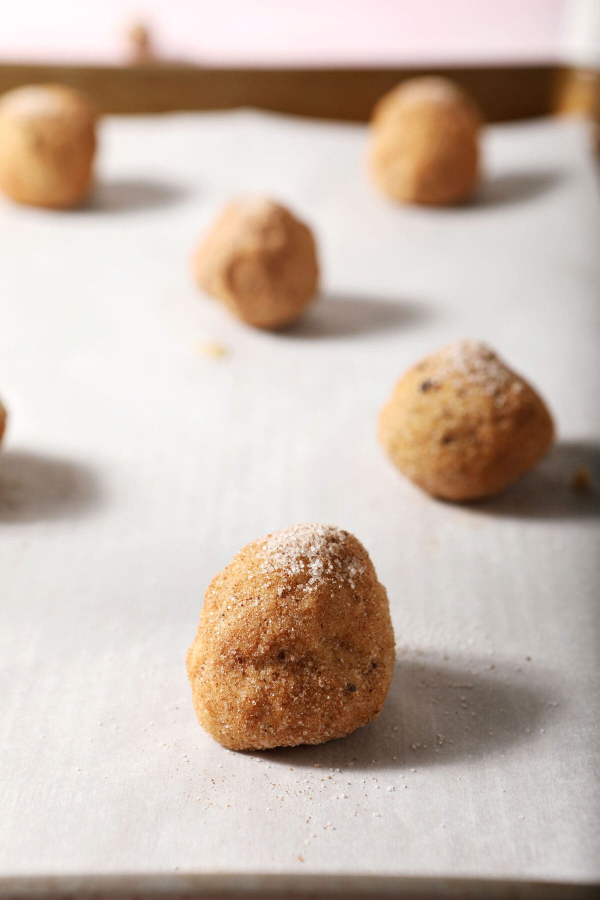 Cookie dough balls rolled in sugar and spices before baking on a lined sheet pan