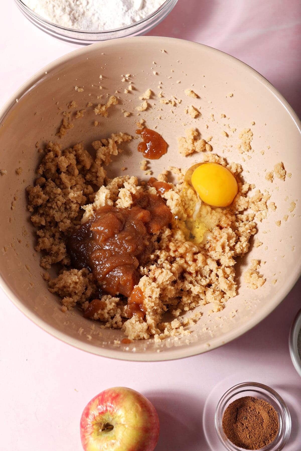 Apple butter, egg and vanilla extract on top of creamed butter and sugar in a bowl on a pink surface