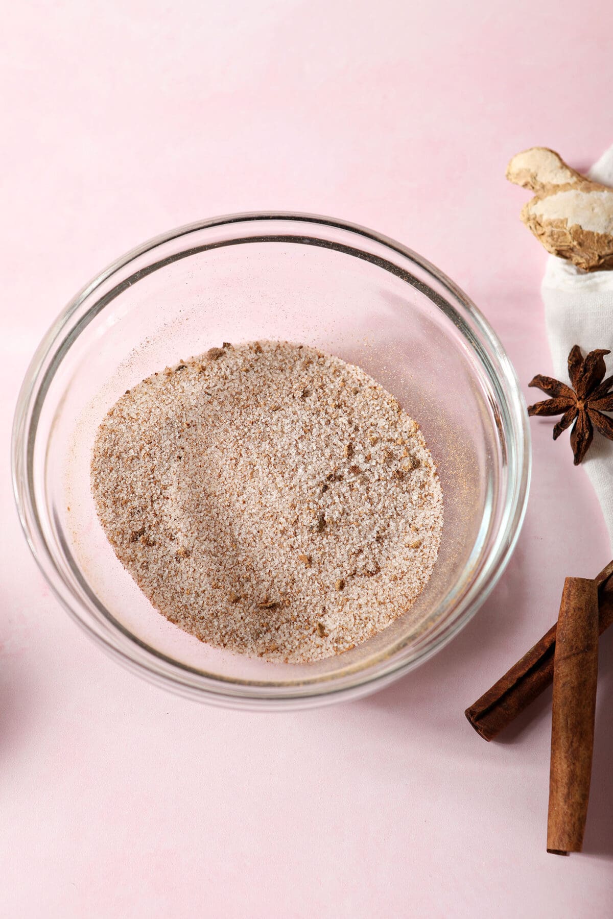The spice mixture for apple butter snickerdoodles in a bowl next to whole spices on a pink surface