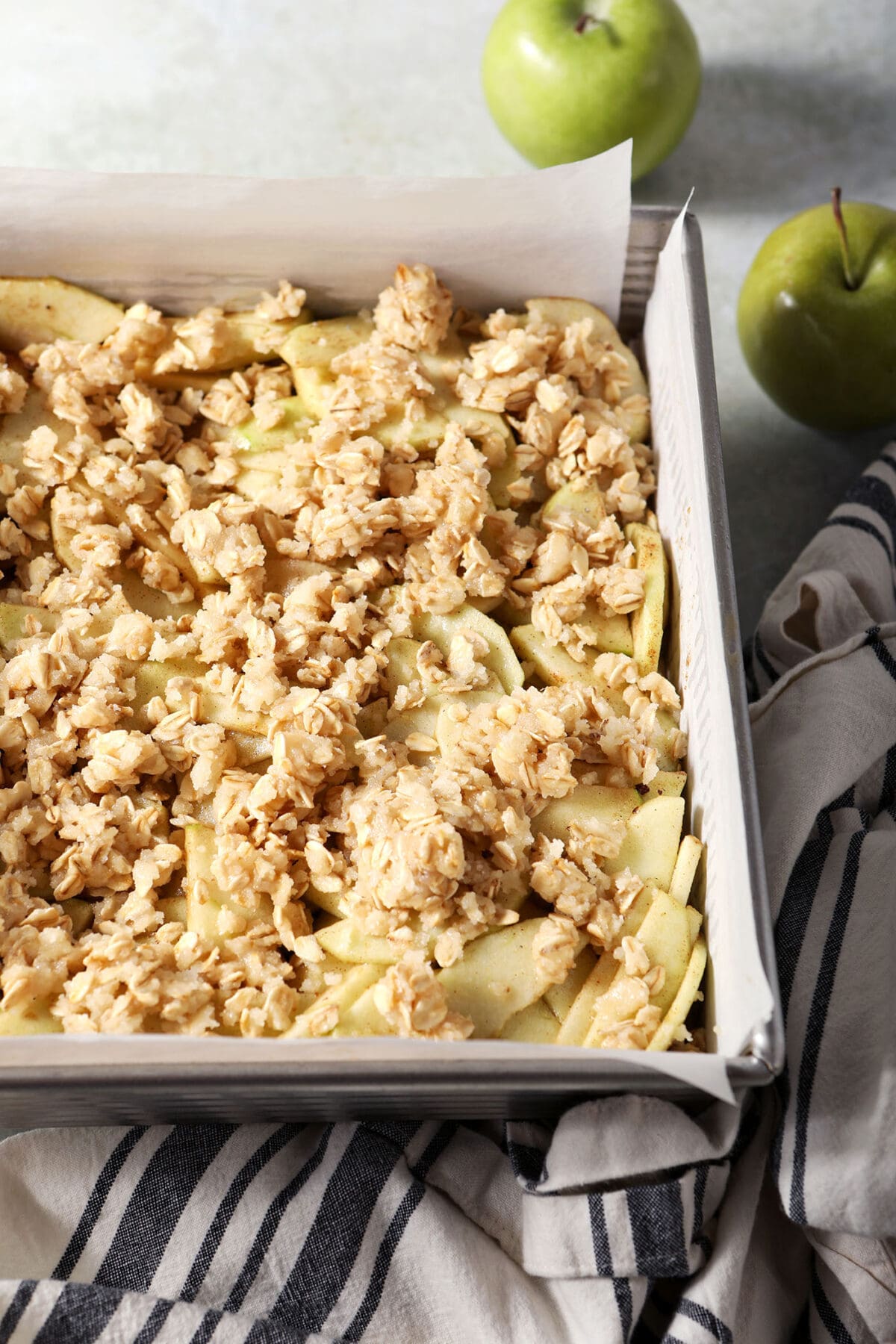 The crumb topping on top of apples in a square baking dish before baking