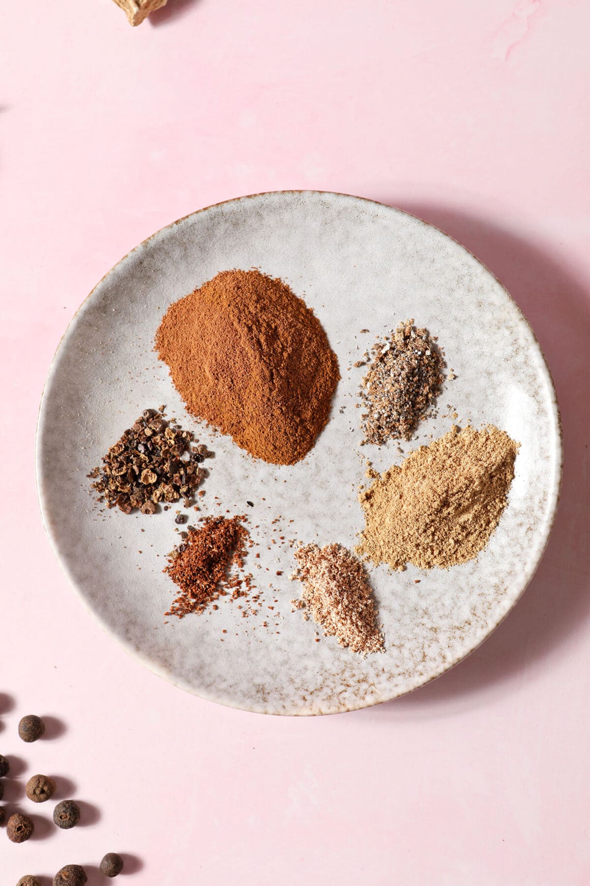 close up of a plate of ground spices before combining them on a pink surface