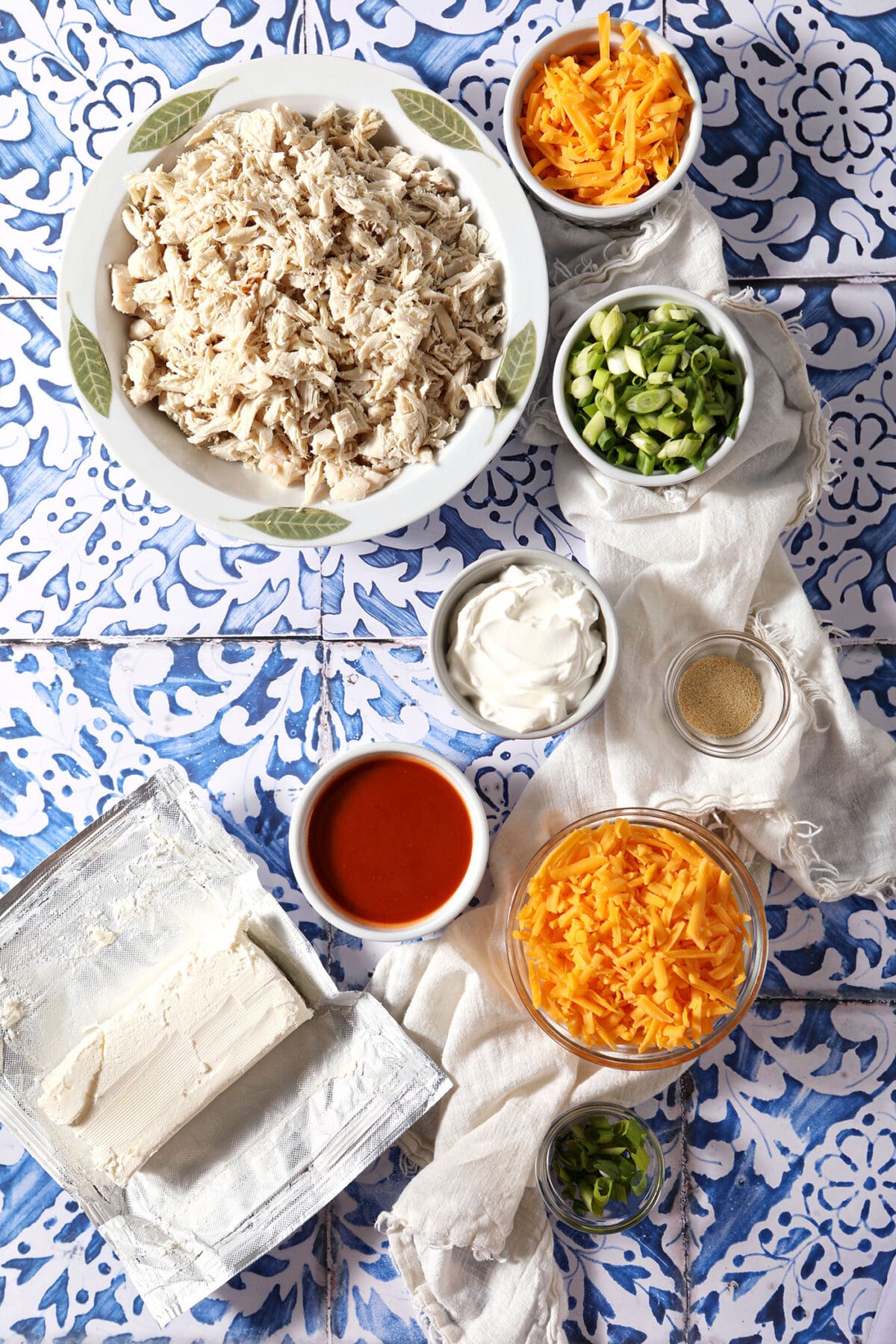 Ingredients to make Buffalo Chicken Dip in bowls on a blue tiled surface