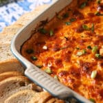 A square baking dish of buffalo dip next to baguette slices