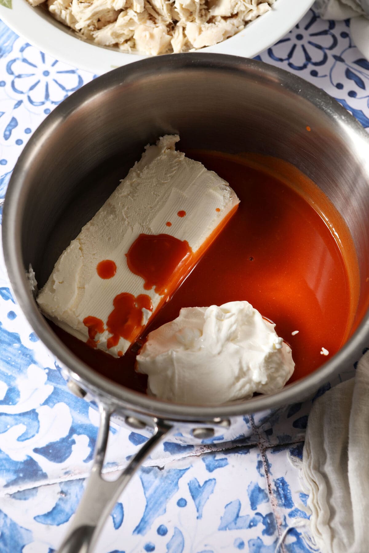Sour cream, cream cheese and hot sauce in a sauce pan on a blue and white tiled surface