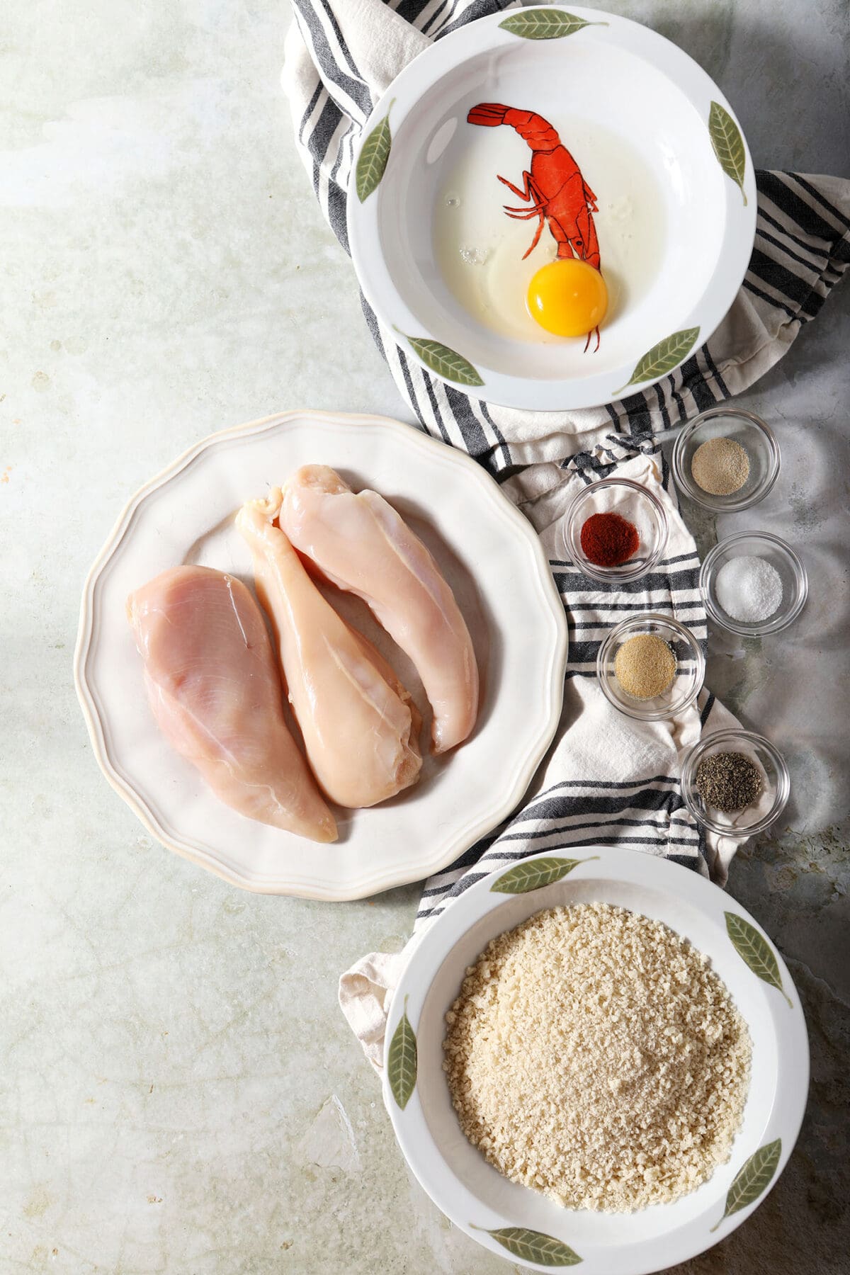 Ingredients to make chicken nuggets at home in bowls on a green surface with black and white striped linens