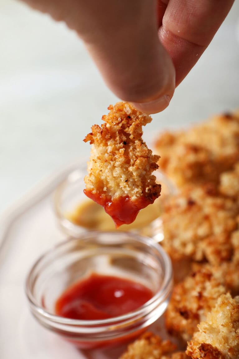 A hand dips a chicken nugget into a bowl of ketchup