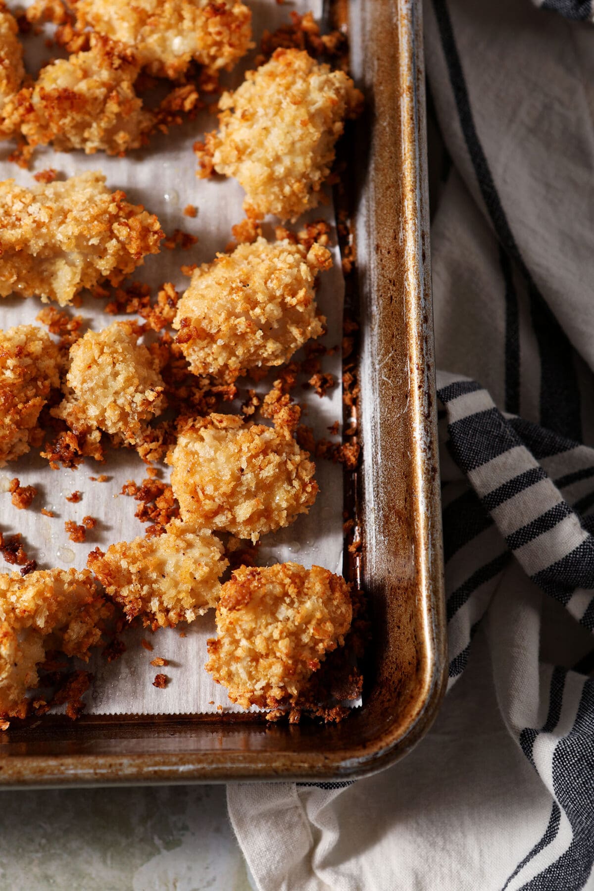 Baked chicken nuggets on a sheet pan on an olive green surface with a black and white striped linen