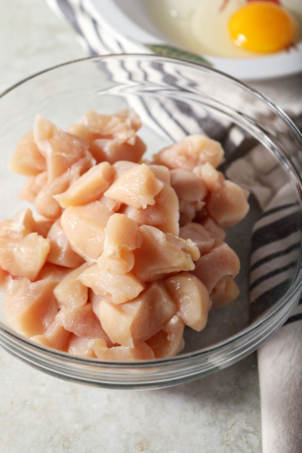 Chopped chicken breasts in a glass bowl on an olive green surface