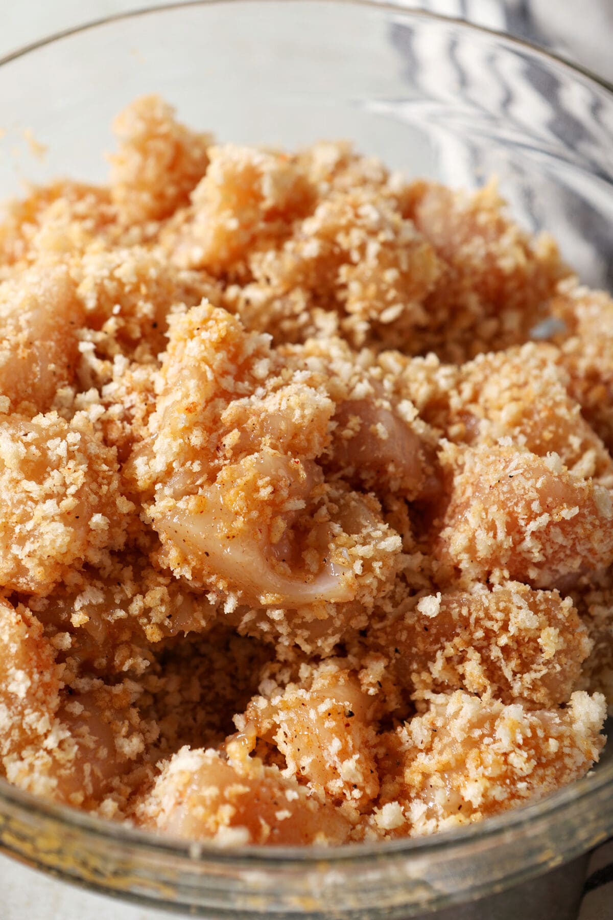 Panko bread crumbs on top of chicken chunks in a glass bowl