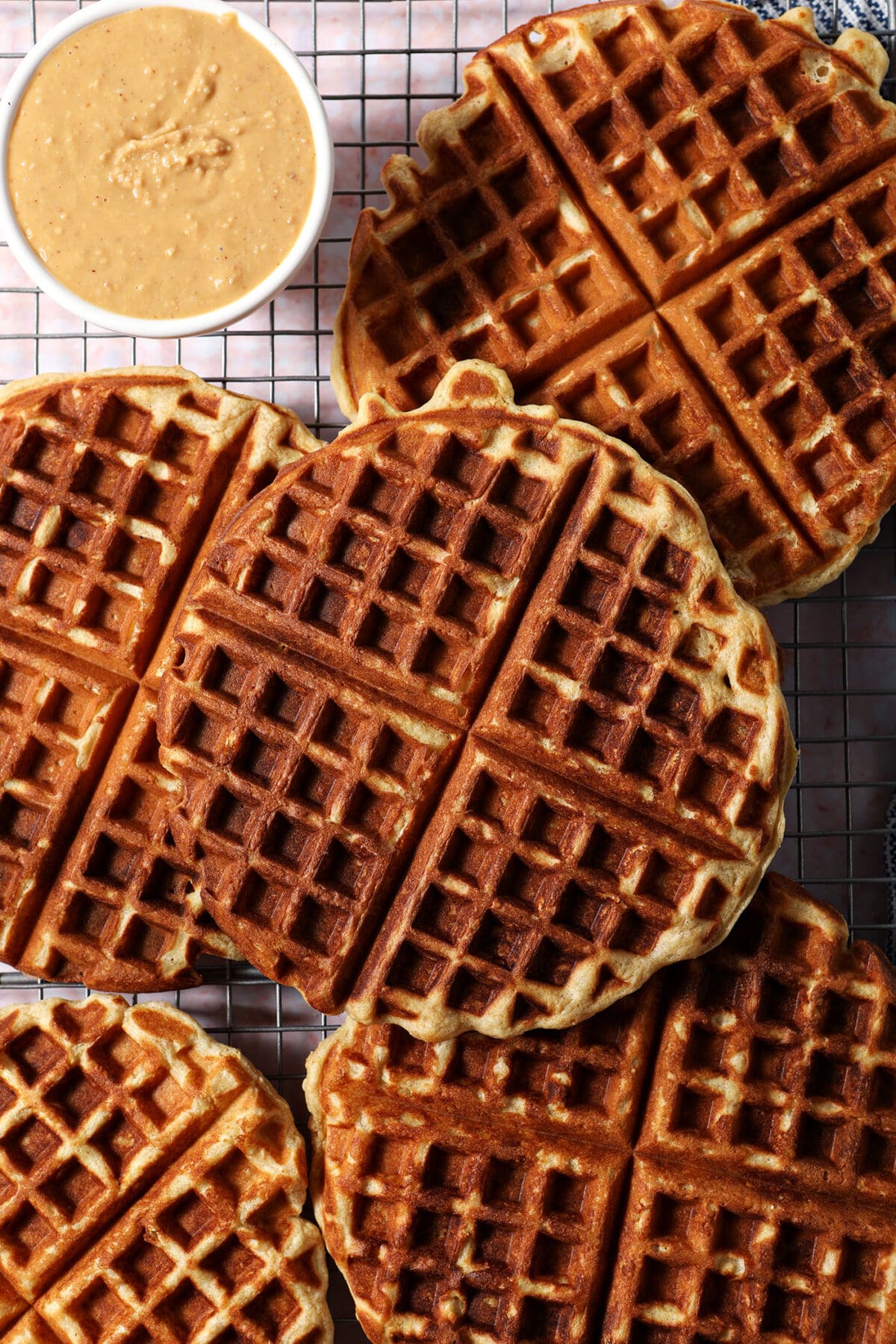 Stacked waffles on a wire cooling rack with a bowl of peanut butter