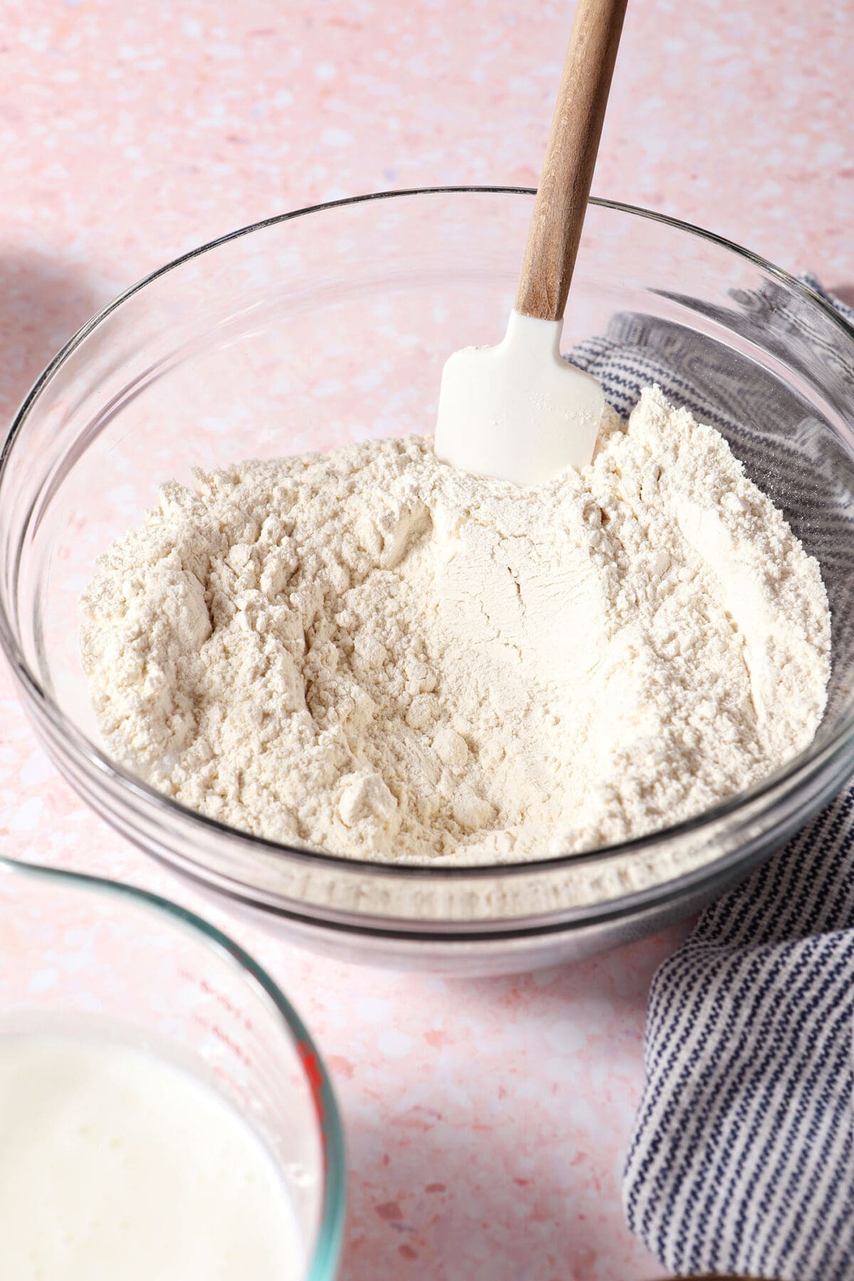 Dry ingredients in a bowl with a rubber spatula on a pink surface