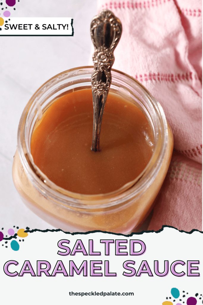 A mason jar of salted caramel sauce on a white tiled surface with a spoon inside it next to a pink linen with the text salted caramel sauce