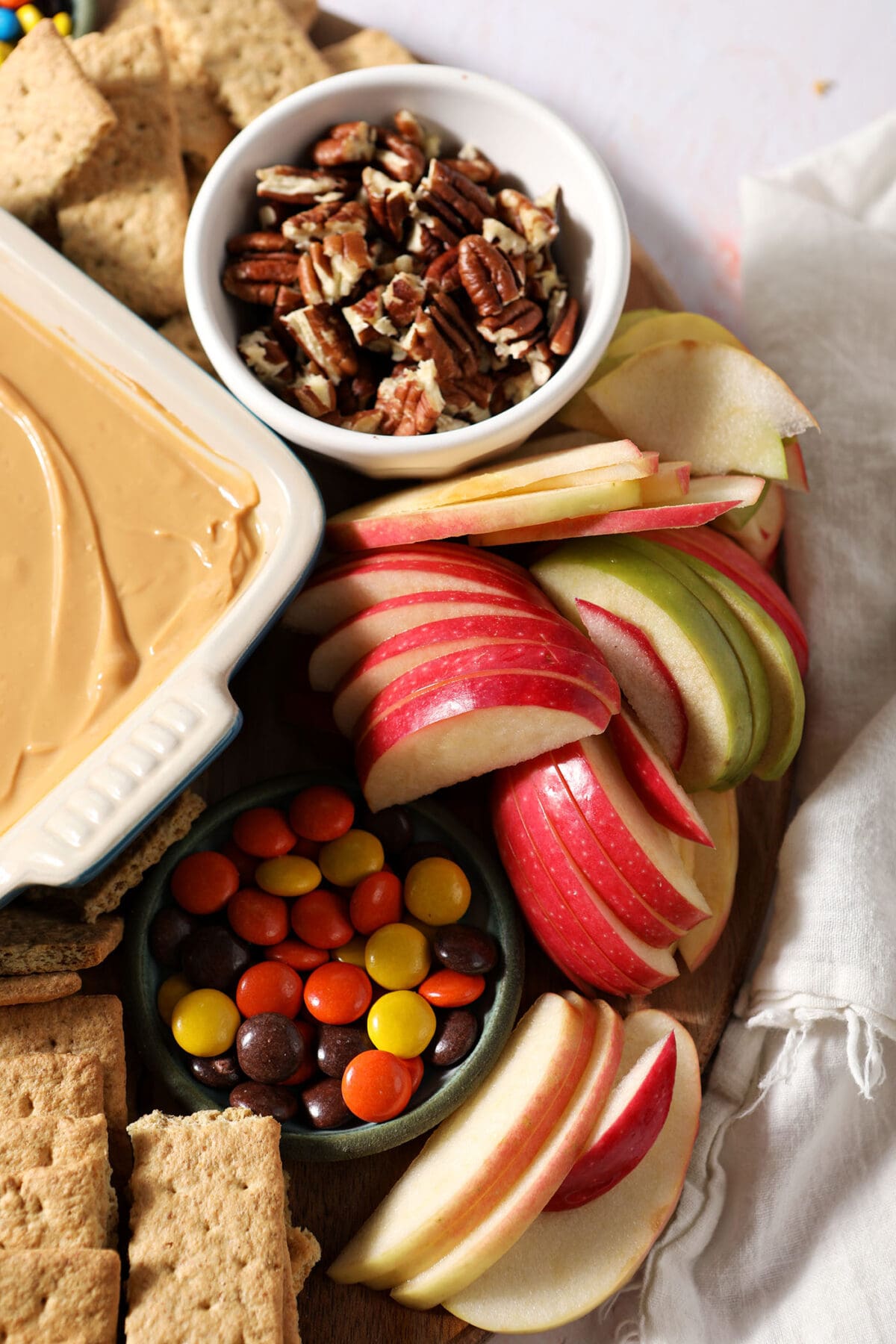 Close up of apple slices, candies and nuts on bowls on a caramel apple board