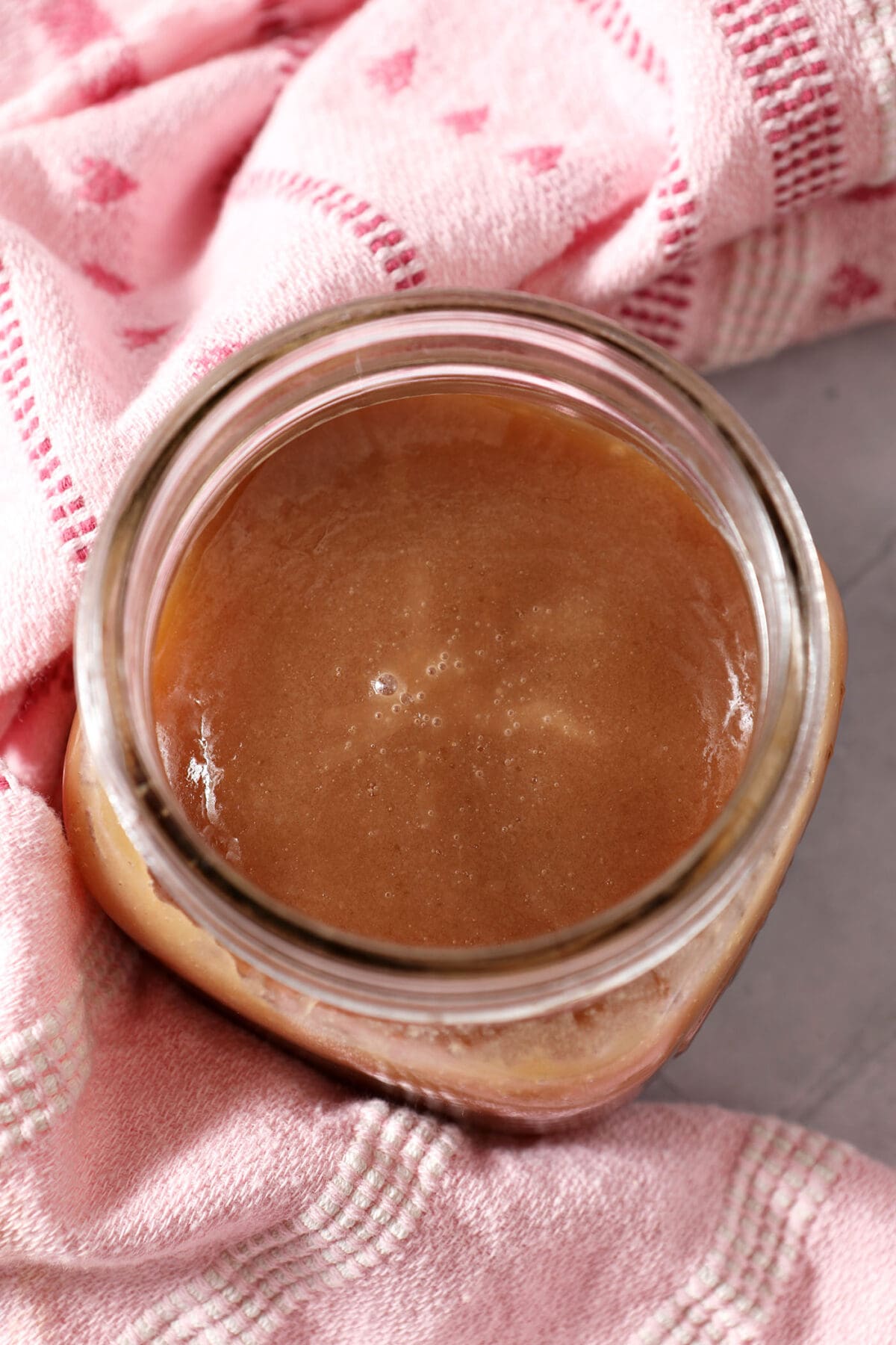 A mason jar of salted caramel sauce surrounded by a pink linen