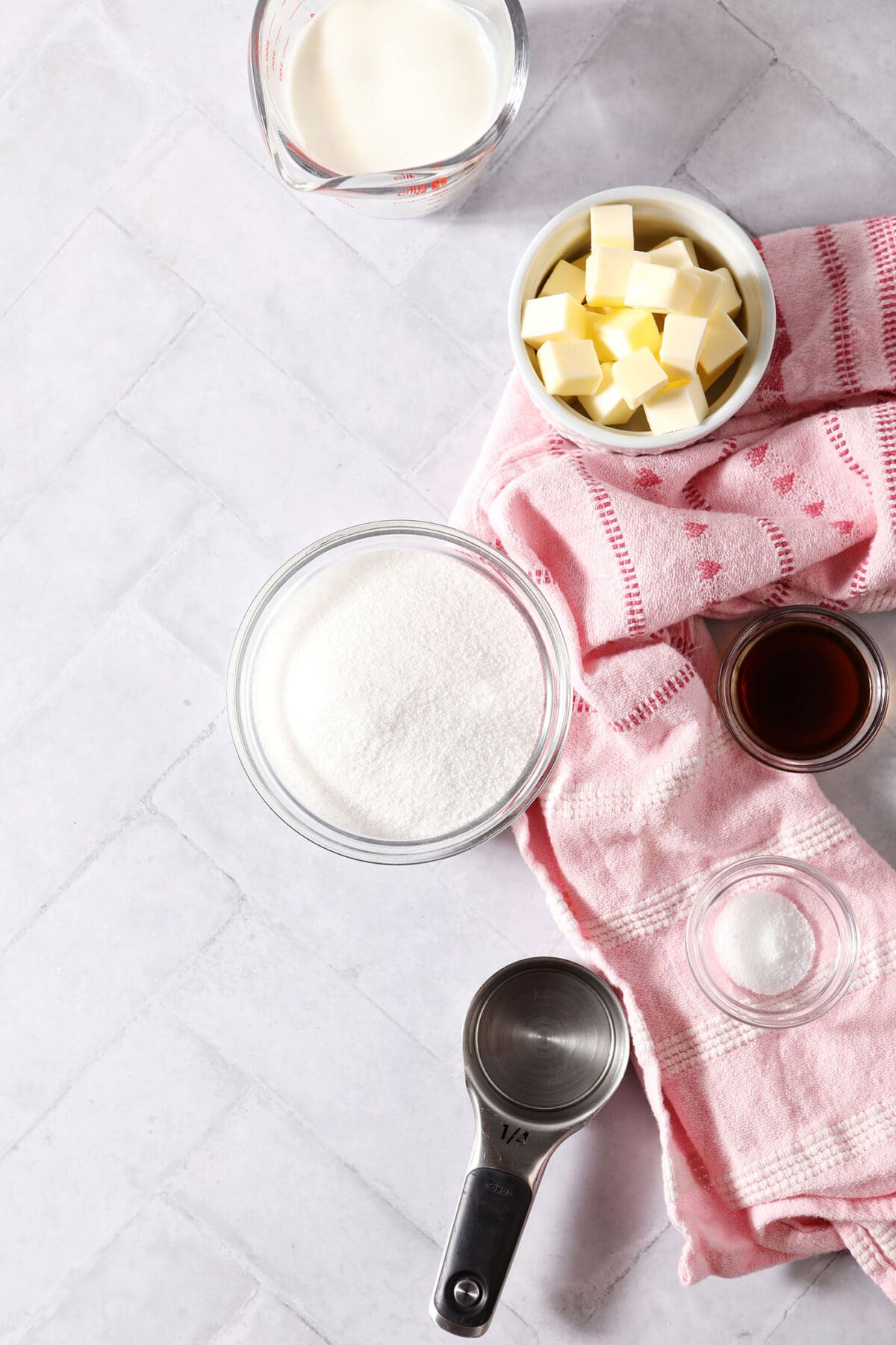 Ingredients to make salted caramel sauce in bowls and cups on a tiled surface with a pink linen