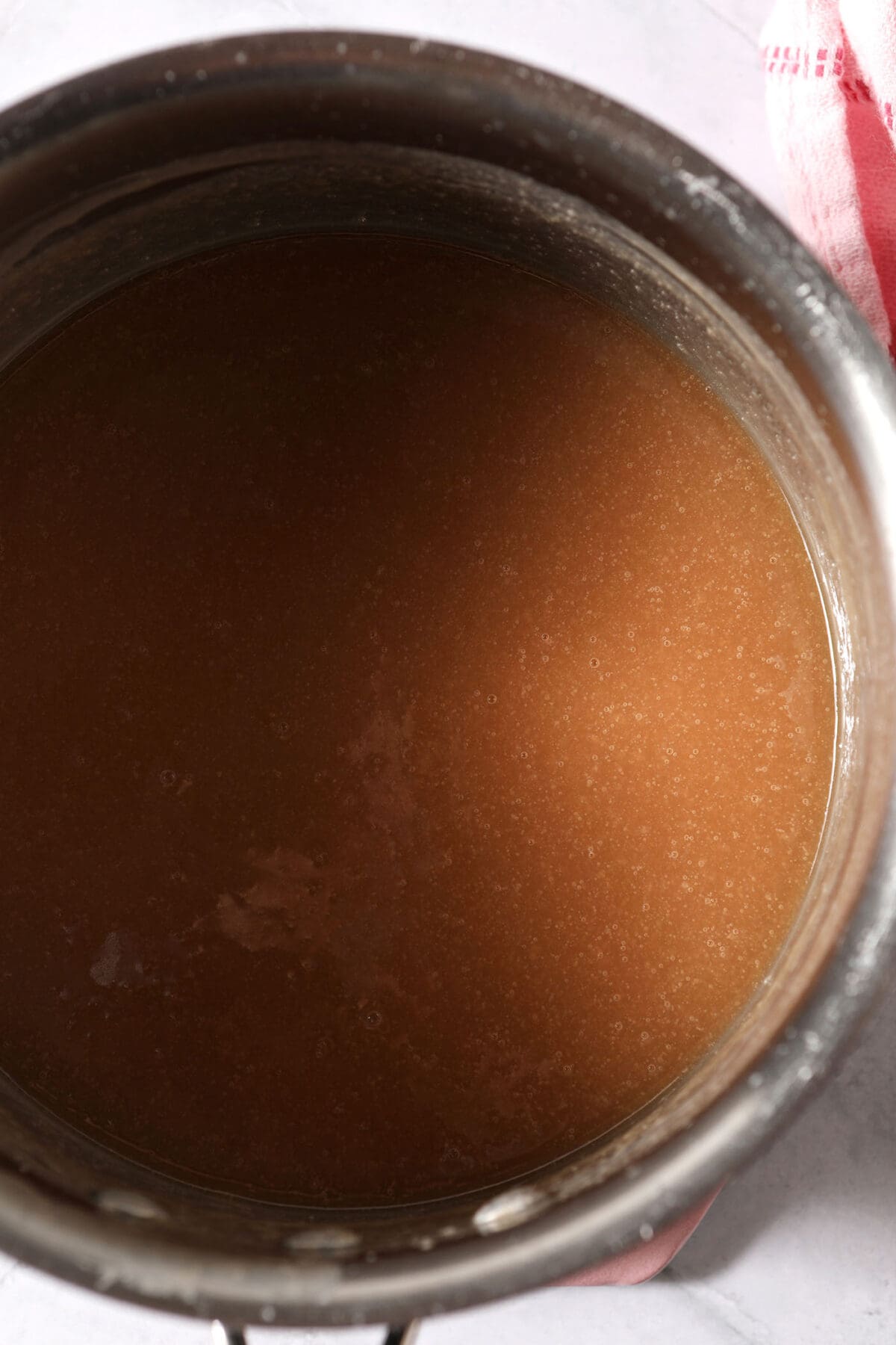 A salted caramel sauce in a saucepan on a white surface next to a pink linen