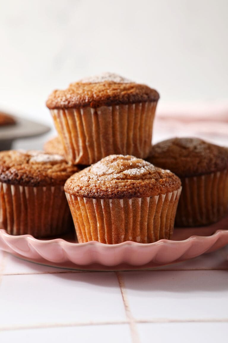 A pink plate holds a stack of apple cider muffins stacked on top of each other