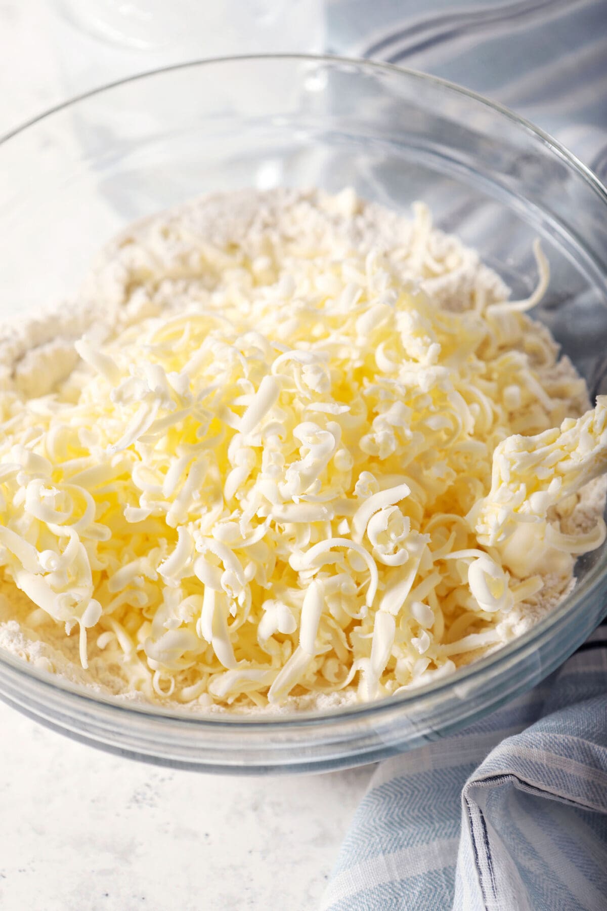 Shredded butter on top of dry ingredients in a bowl next to a blue striped linen