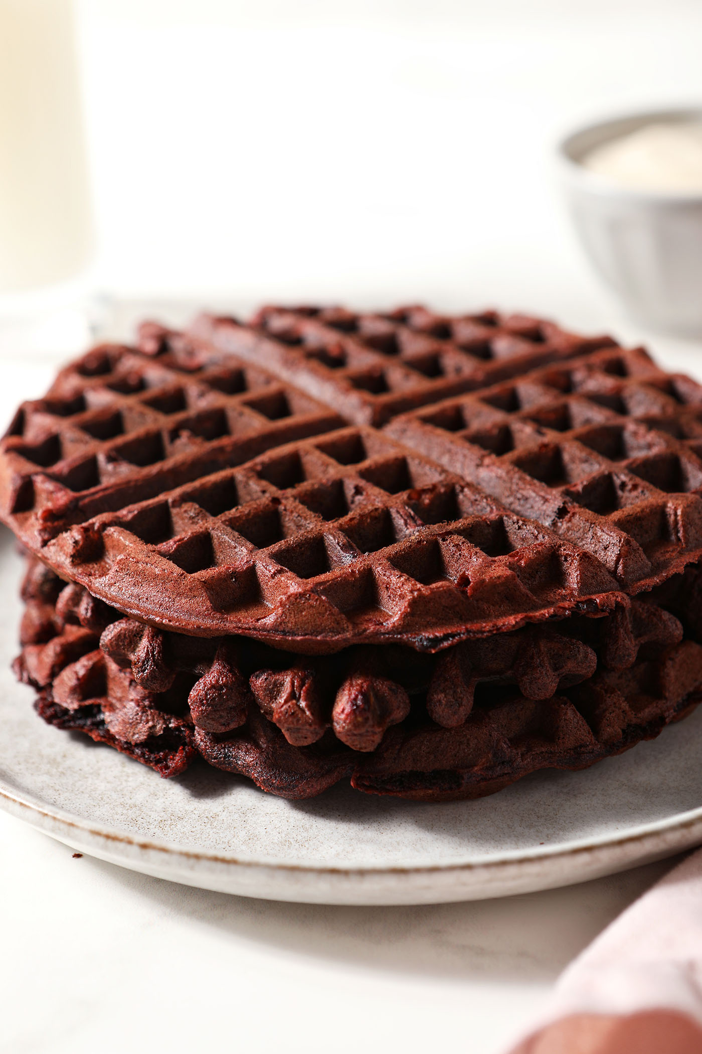 A stack of red velvet waffles on a grey plate next to a pink linen
