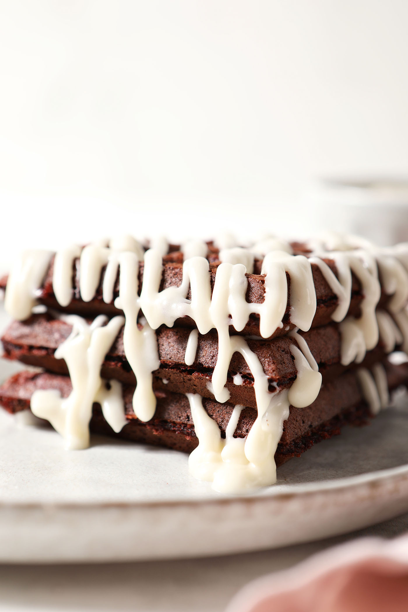 Side angle of a stack of brick red waffles drizzled with cream cheese frosting