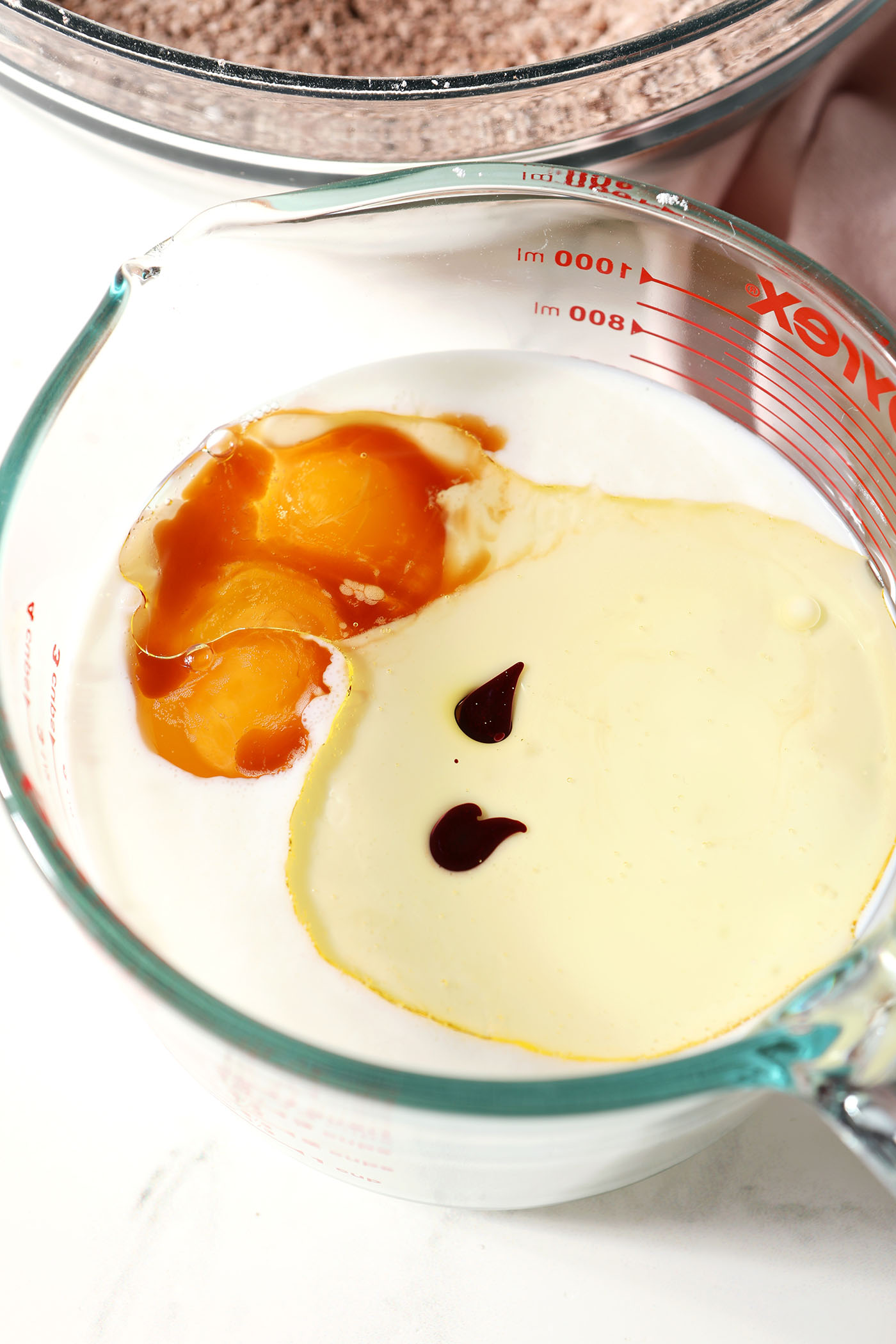 Wet ingredients in a large liquid measuring cup next to dry ingredients on a white surface