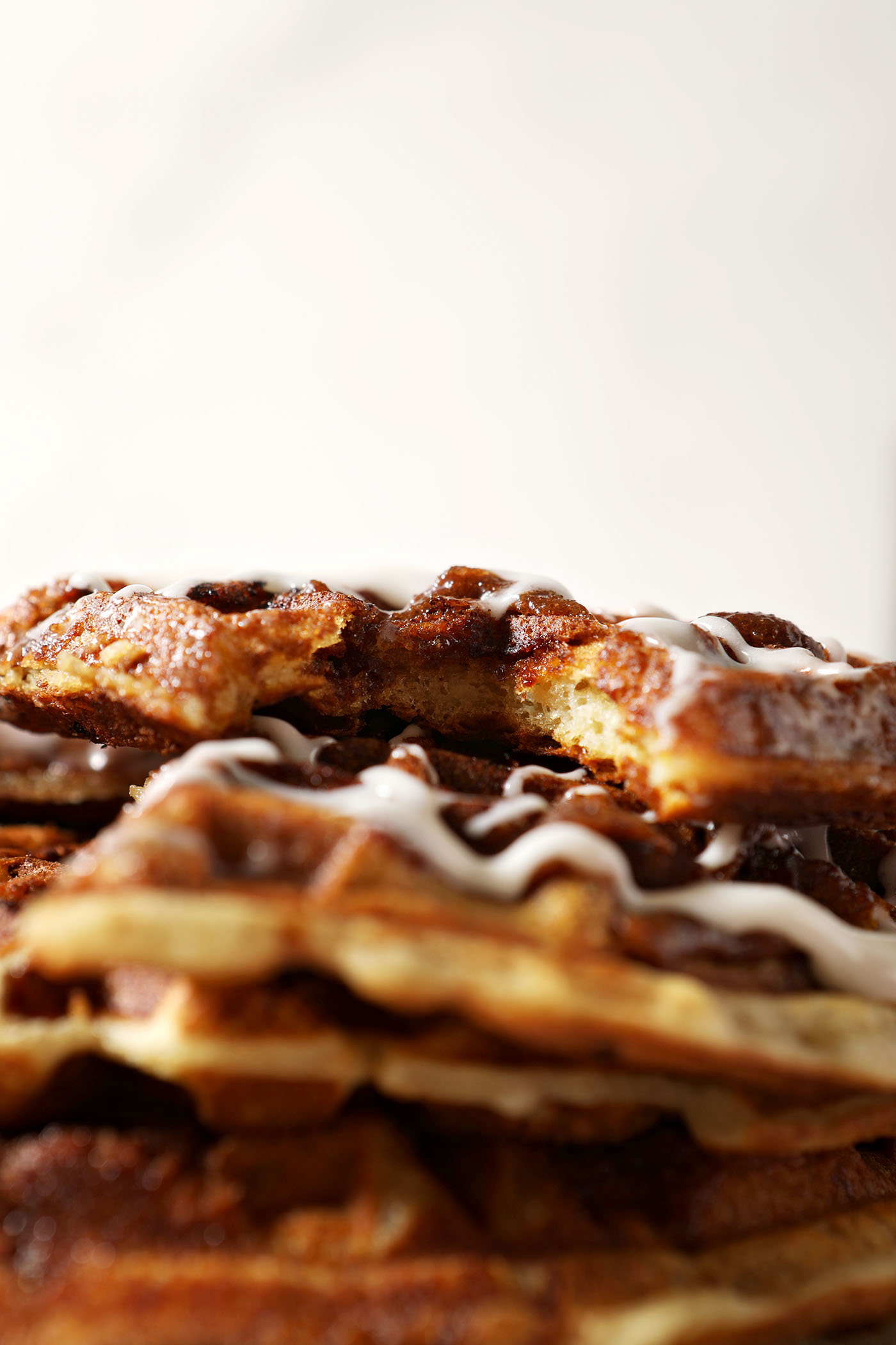 A bitten into Cinnamon Roll Waffle on top of a stack of other waffles