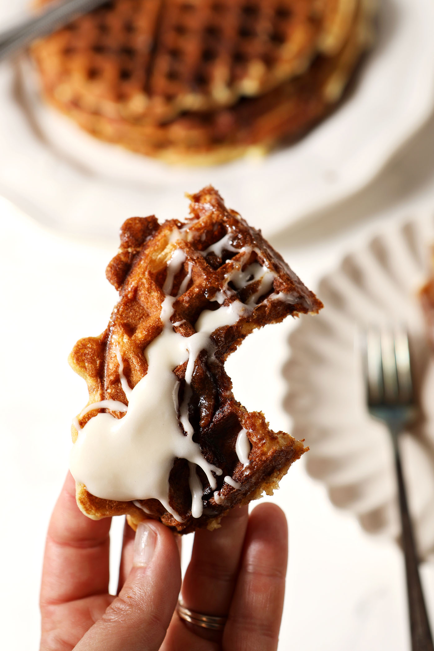 A hand holds a bitten-into quarter of a Cinnamon Roll Waffle topped with cream cheese icing