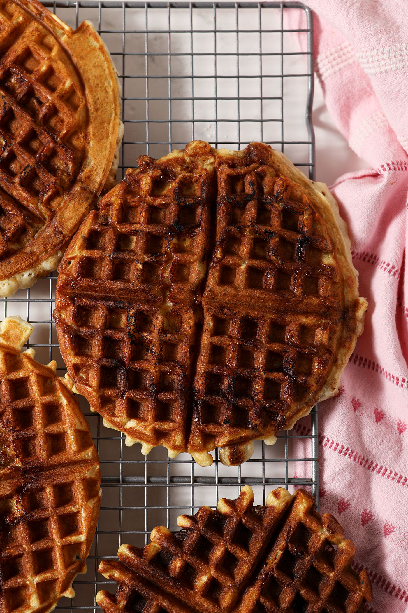 Cooked Cinnamon Roll Waffles on a wire cooling rack next to a pink linen