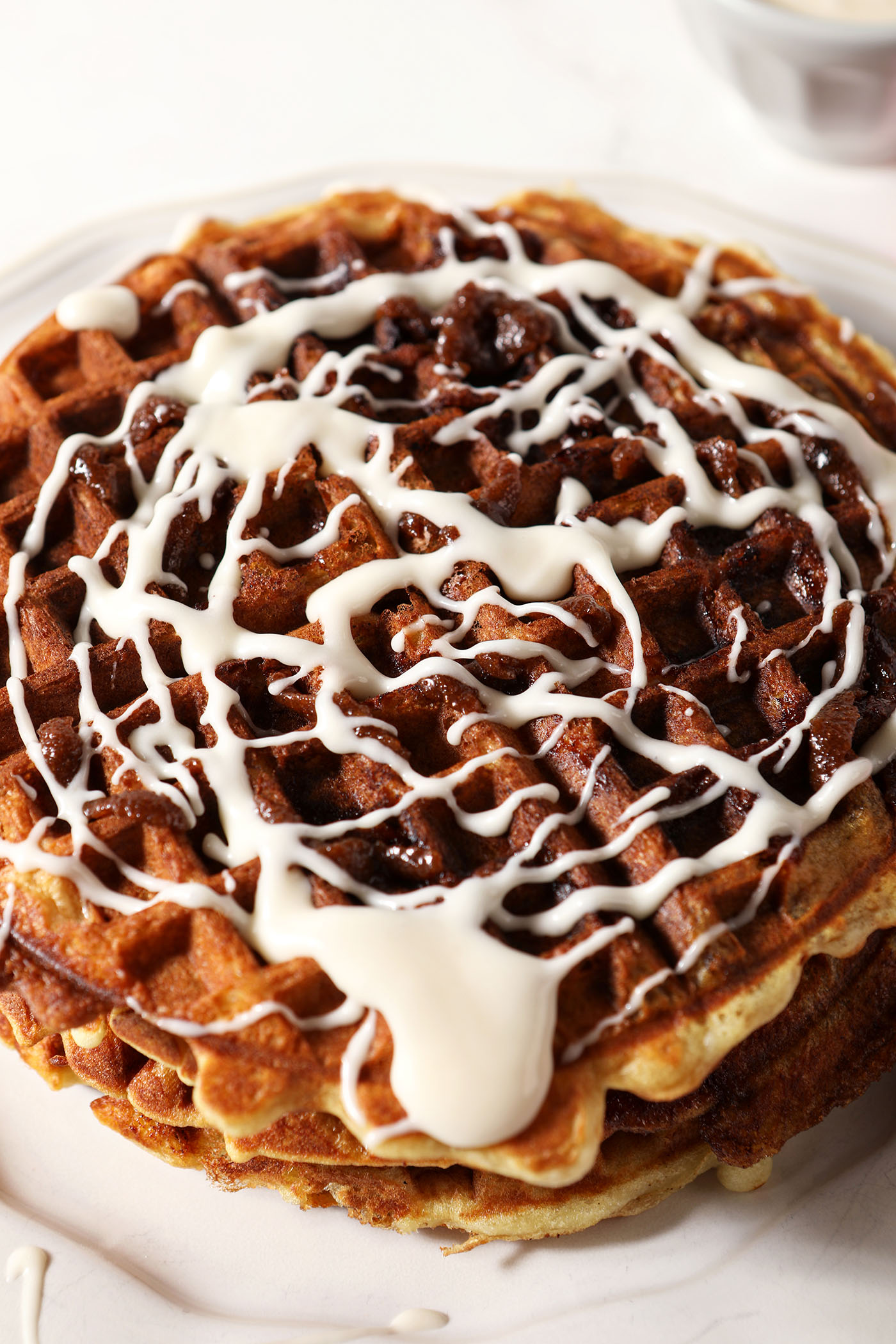 Close up of a stack of Cooked Cinnamon Roll Waffle topped with cream cheese icing