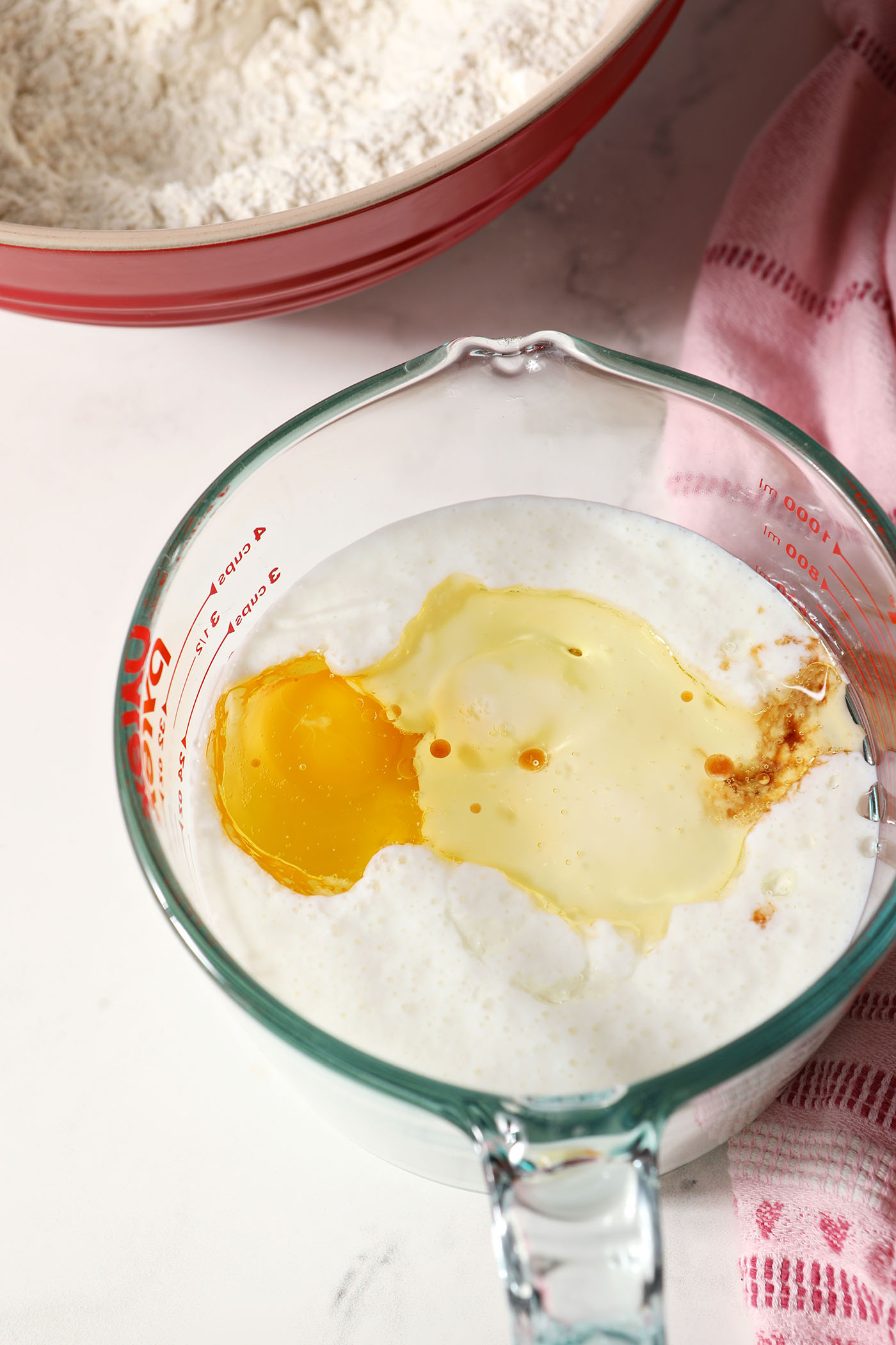 Wet ingredients for waffles in a liquid measuring cup on a marble surface next to a pink linen