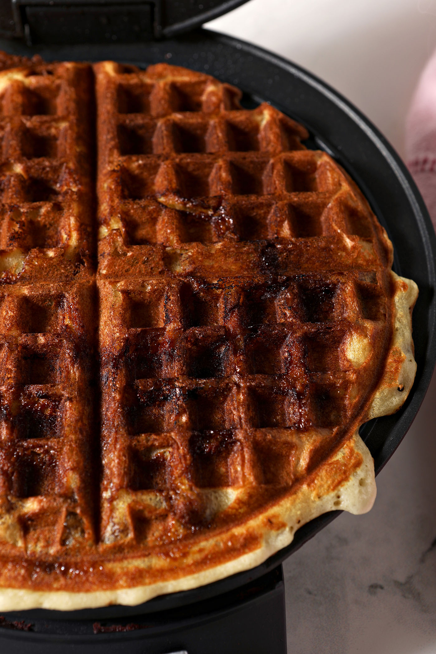 A cinnamon roll waffle cooks in a waffle iron