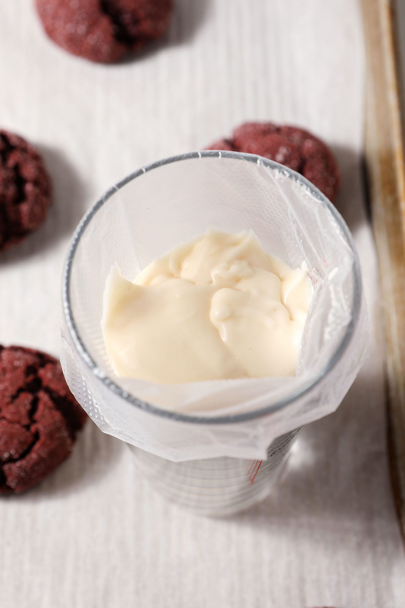 cream cheese icing in a piping bag next to cookies on a sheet pan