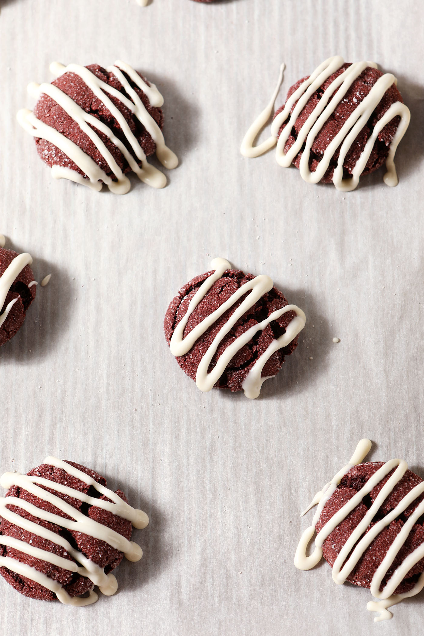 frosted red velvet sugar cookies on a parchment-lined sheet pan