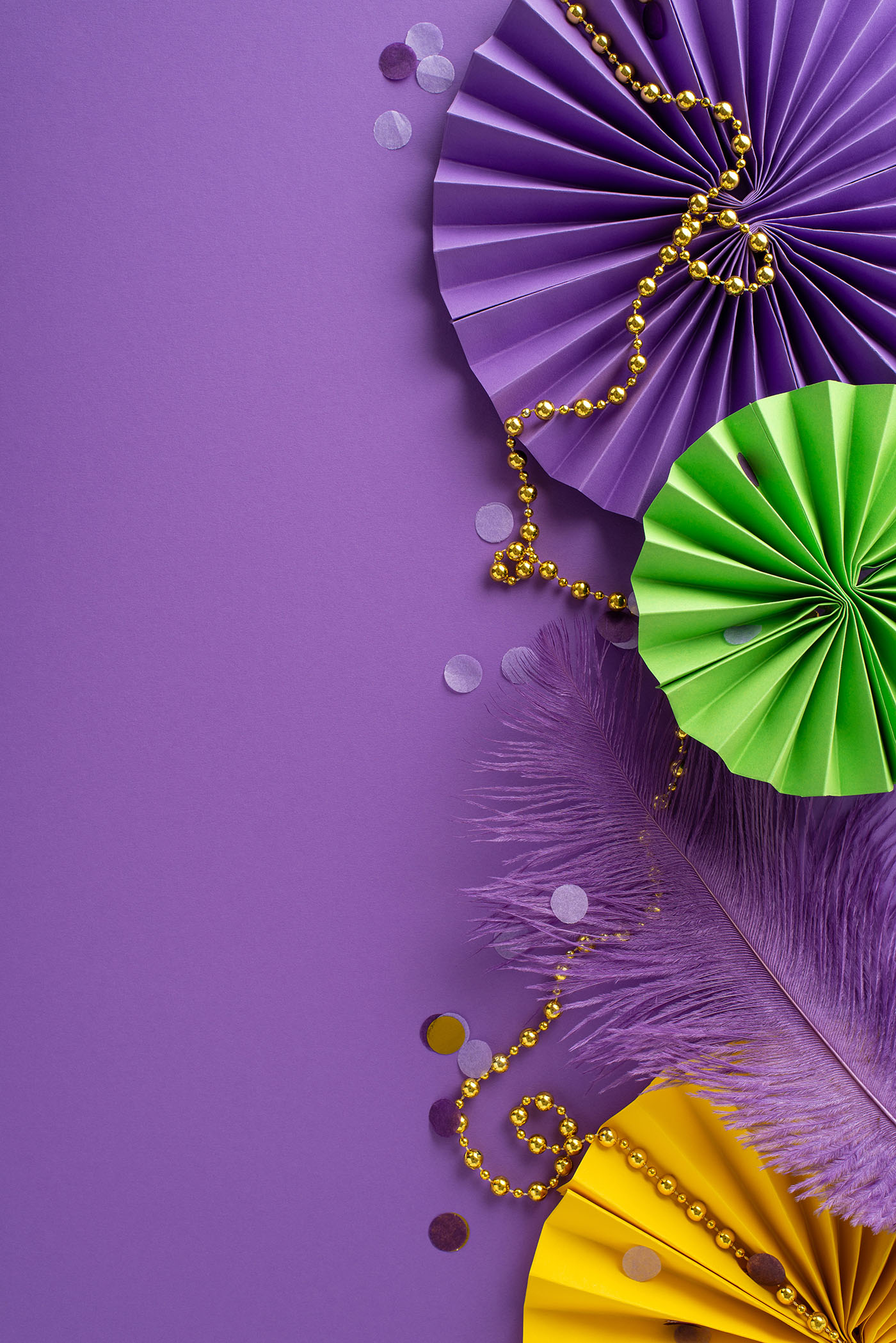 vertical top view festive beads, feathers and more in green, purple and gold on a purple background